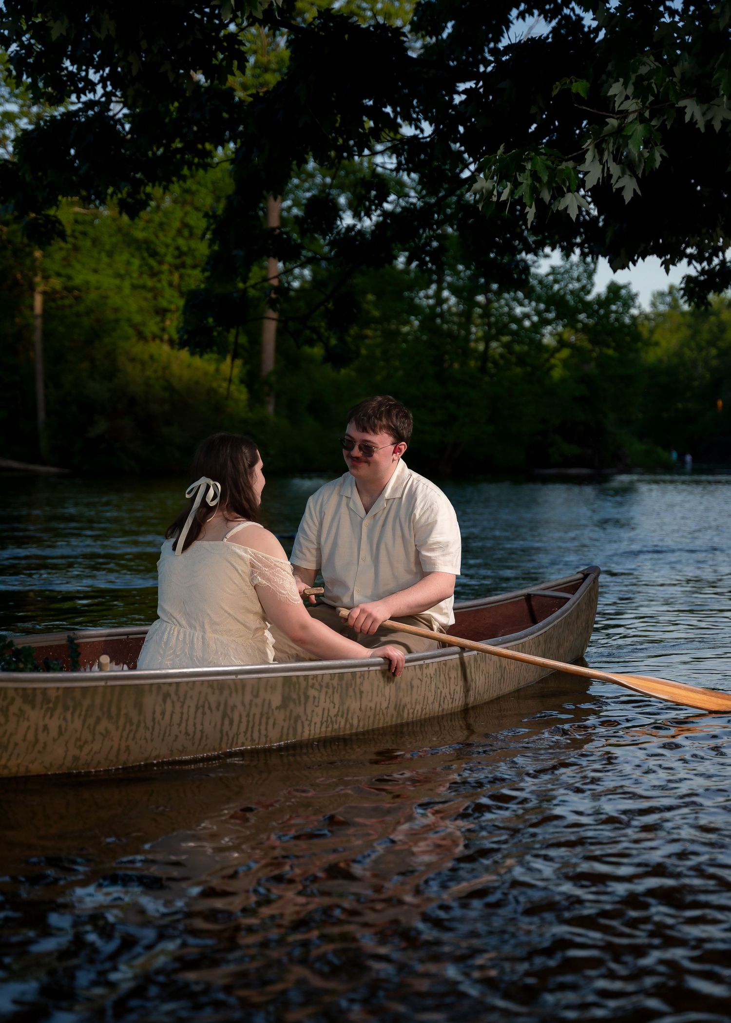 Couple sharing a romantic moment in a wooden rowboat on a serene lake surrounded by lush green trees.