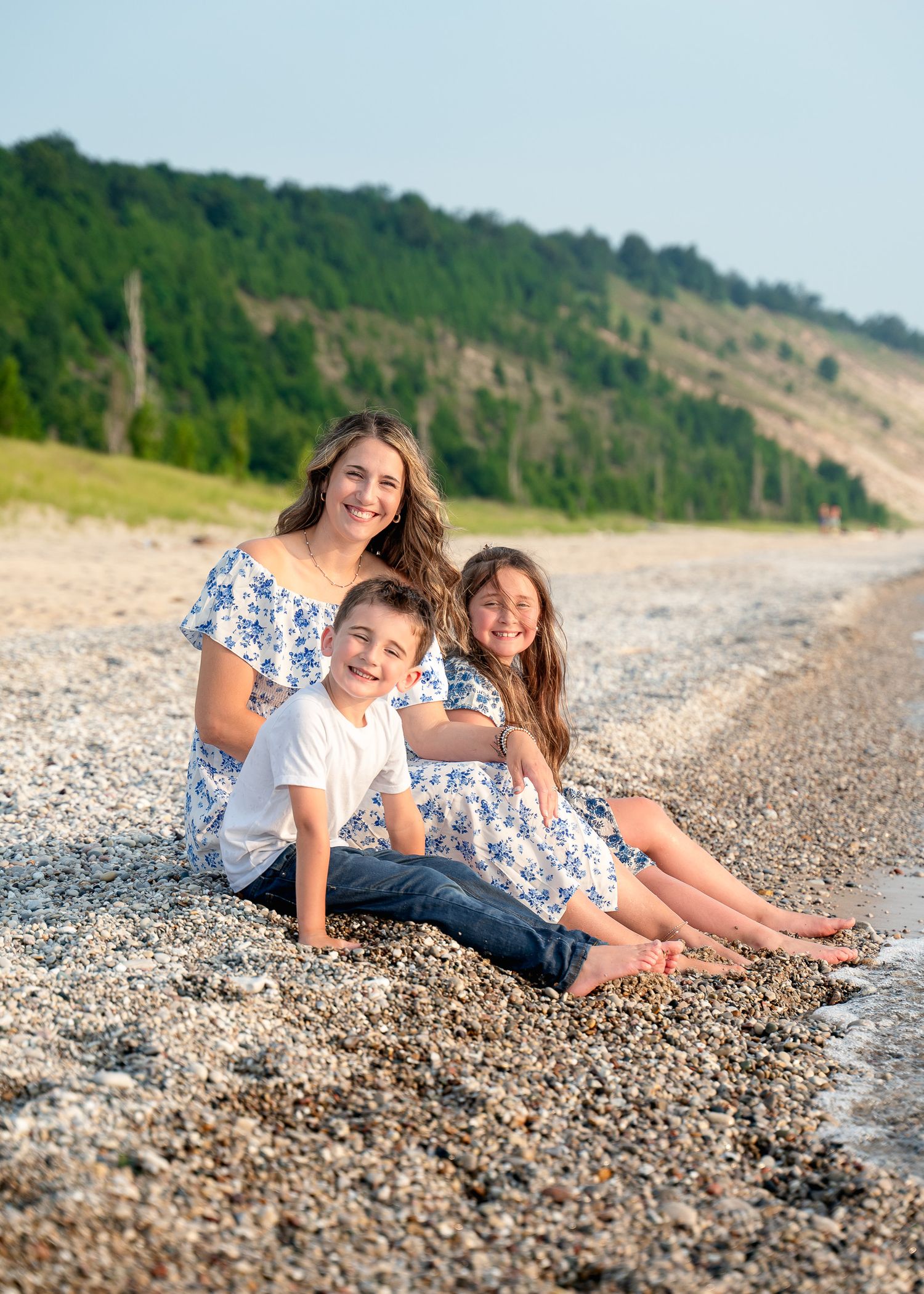 Family members lying together on a rocky beach near wooded cliffs on a sunny day.