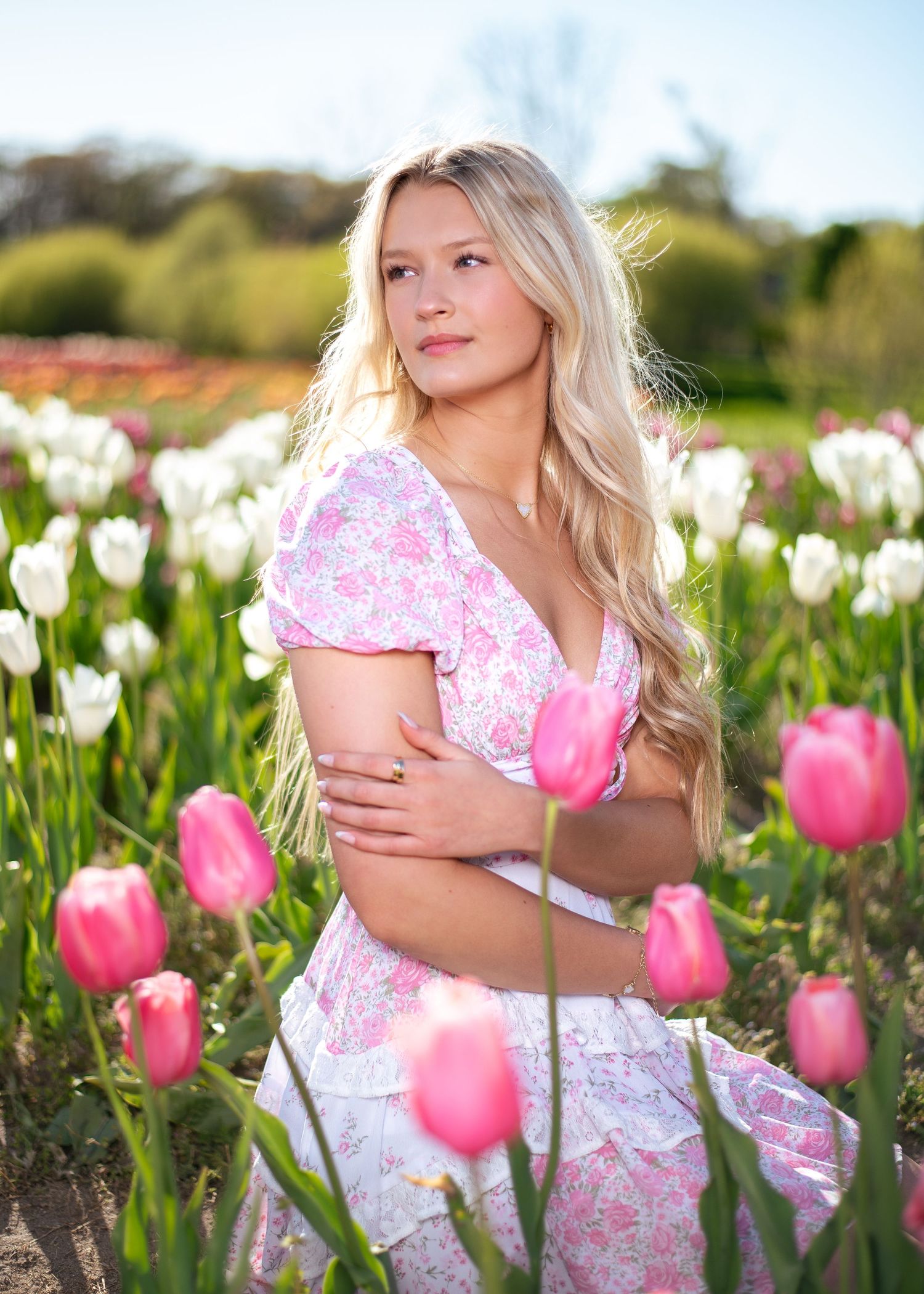 A portrait in a field of pink and white tulips on a sunny day.