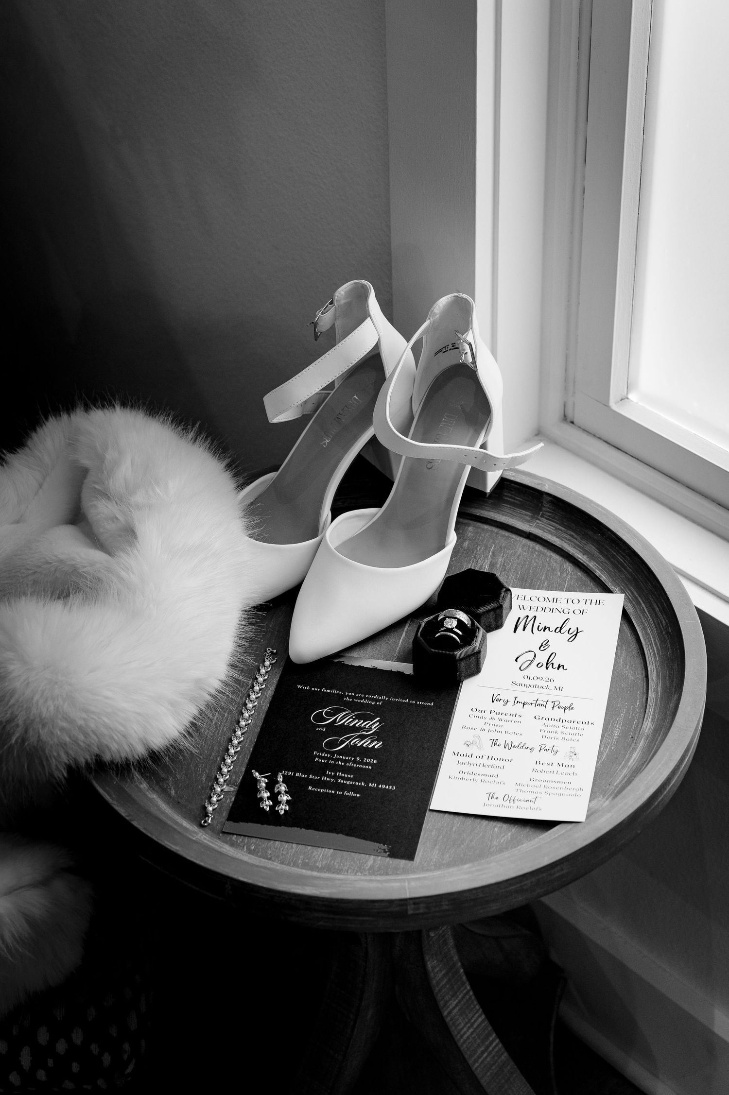 Wedding accessories including white heels, invitations and a fur stole arranged on a windowsill.