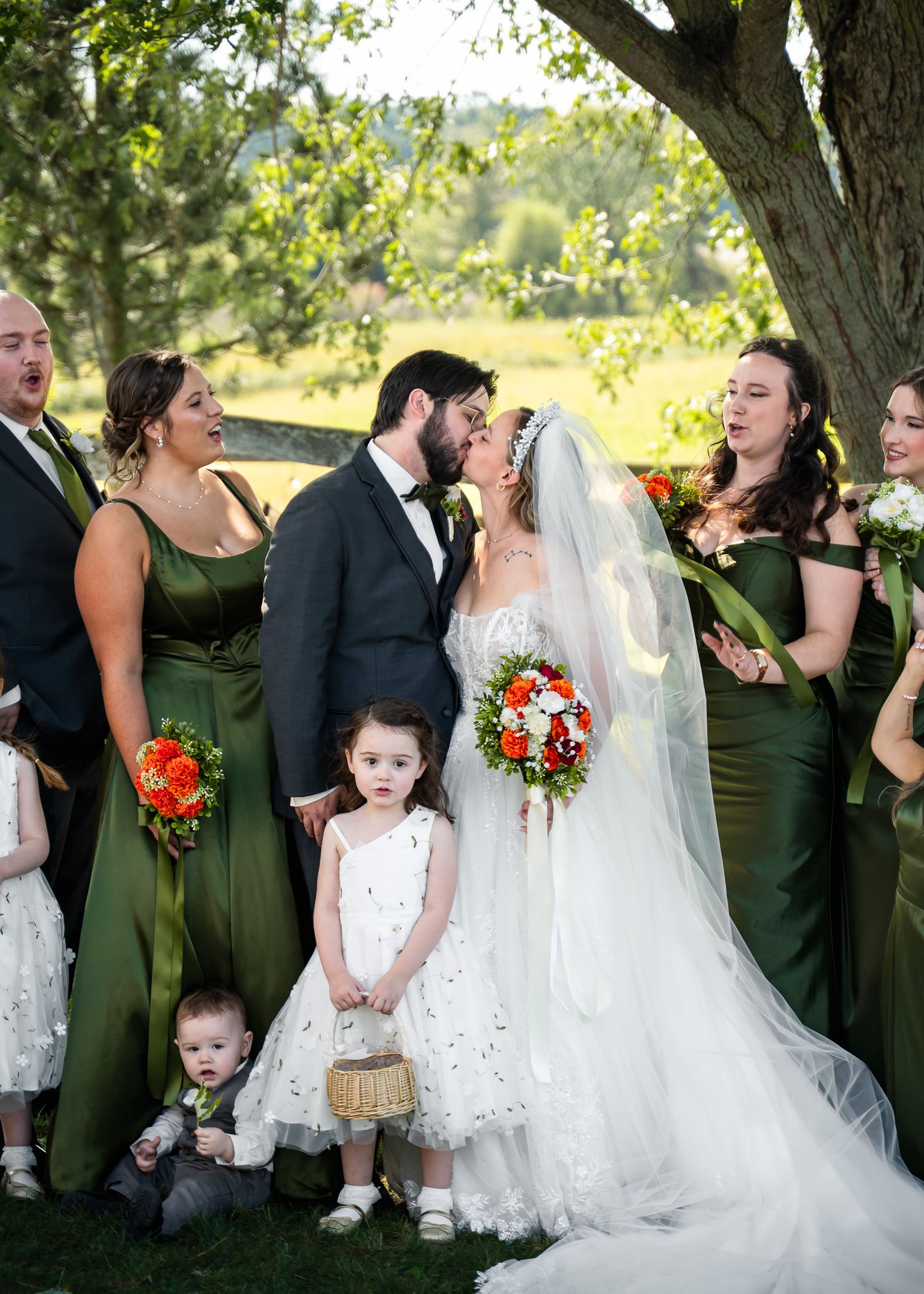 Wedding party gathered under shady tree for candid group photos.