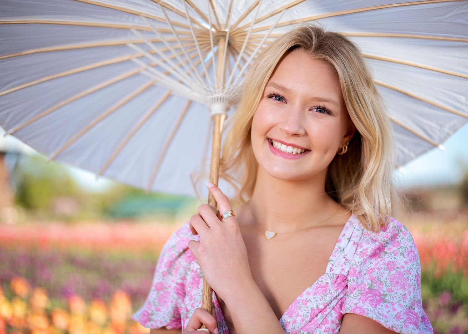 Delicate parasol frames outdoor portrait against blue sky and flowers.
