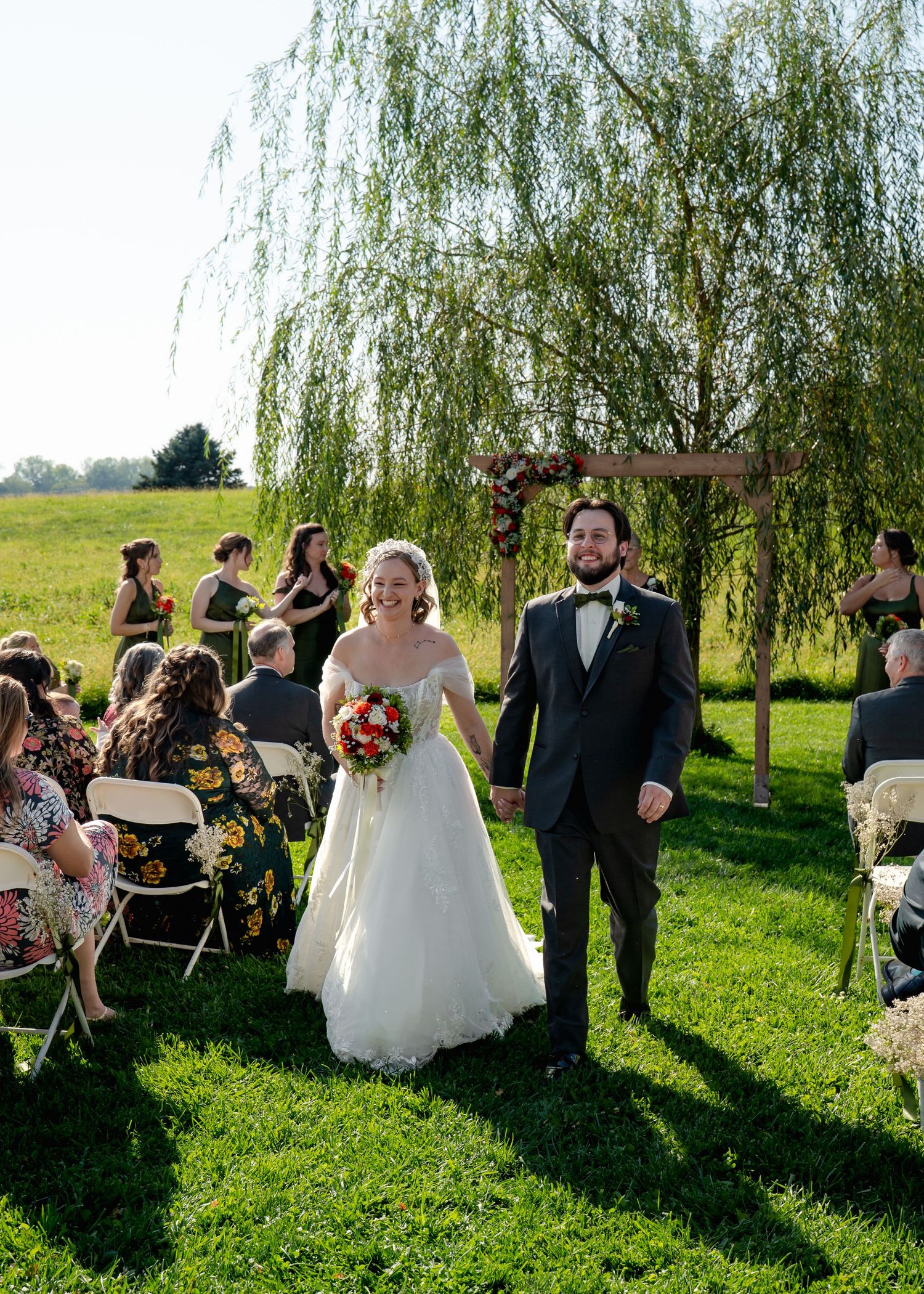 Newlyweds walking down the aisle at an outdoor garden ceremony under a willow tree.