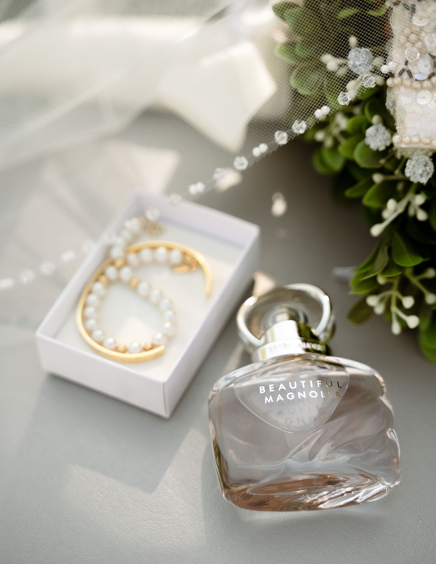 Wedding jewelry and accessories including pearl necklace and perfume bottle on light background.