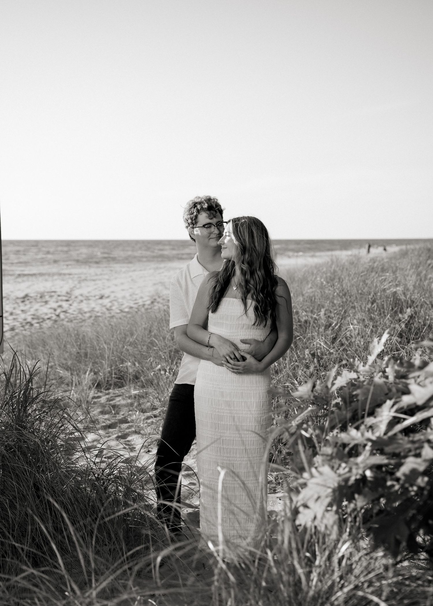 Romantic couple embracing in a grassy field against a bright sky.