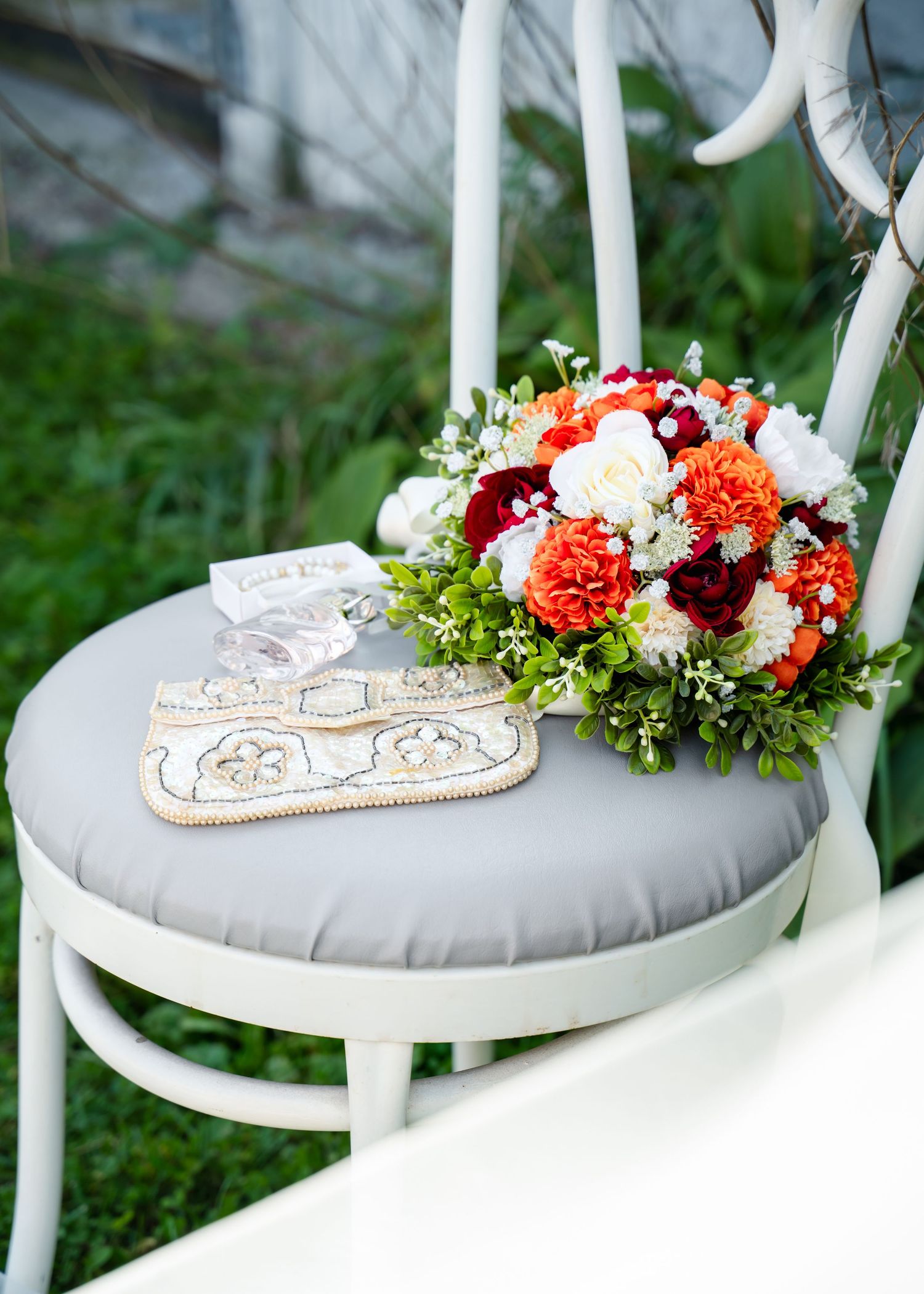 Wedding bouquet with coral and white flowers sits on a gray cushioned chair next to decorative accessories.