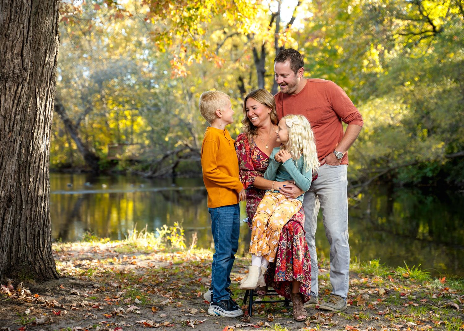 Family portrait session by river with autumn trees and golden light.