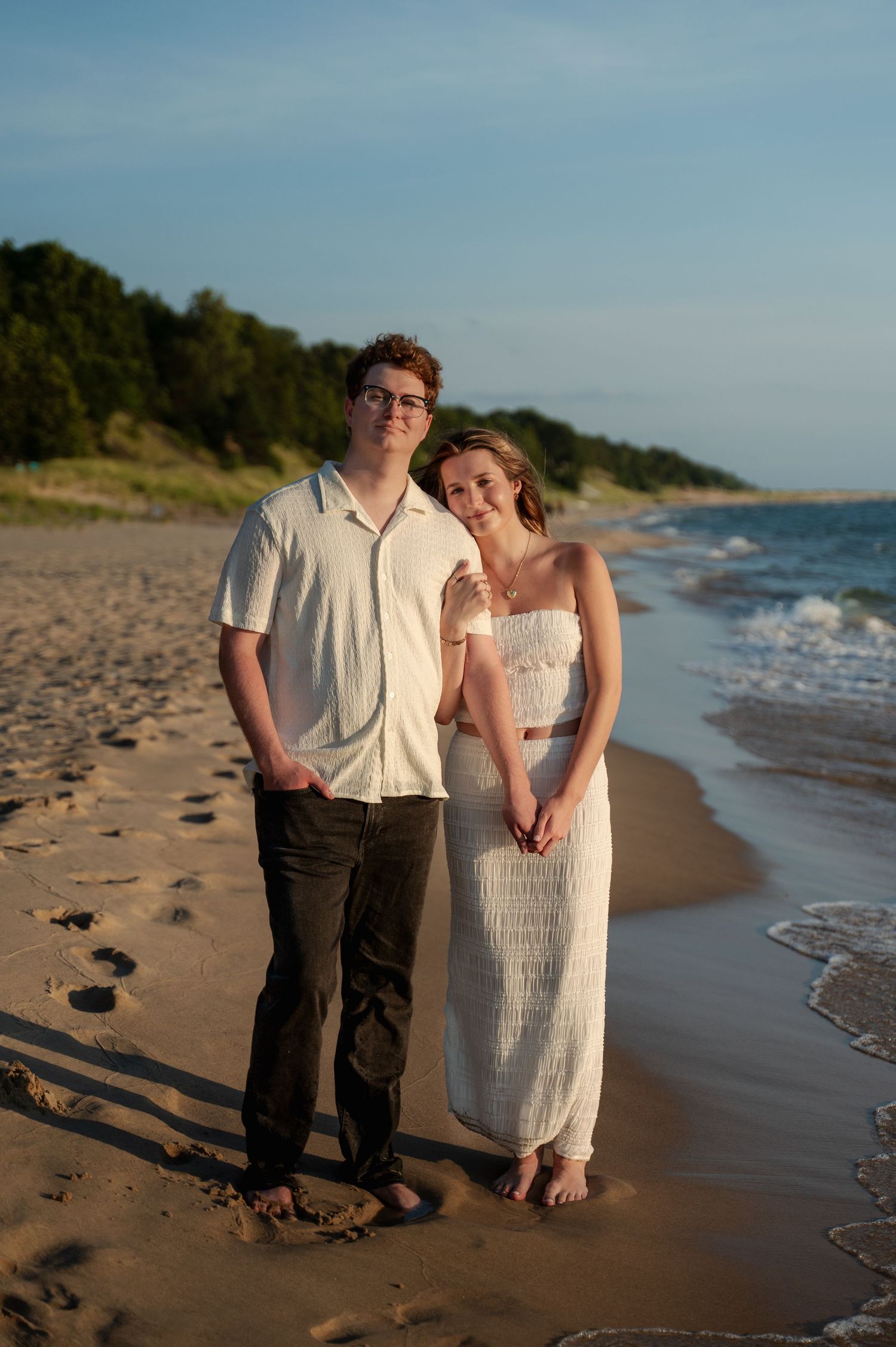 Couple walking hand in hand along shoreline at sunset.
