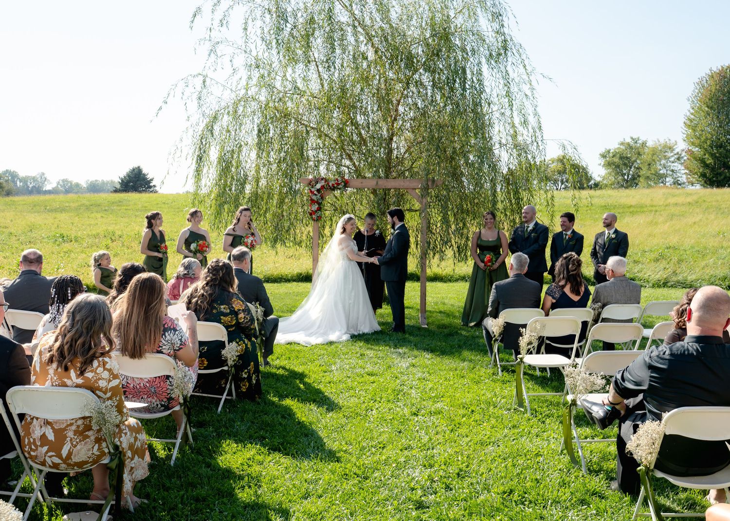 Outdoor garden wedding ceremony with guests seated under a weeping willow tree.