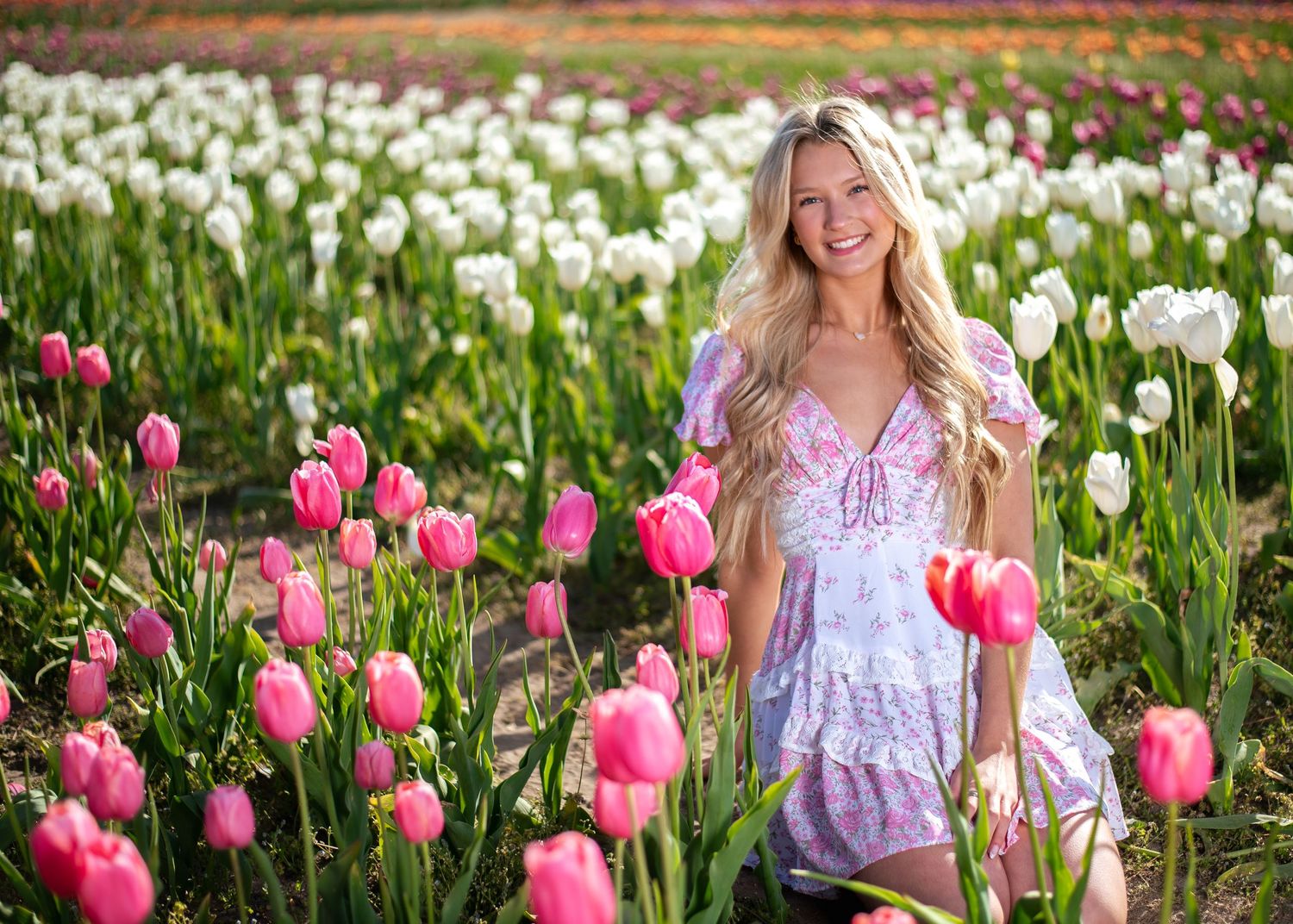 Pink tulips bloom in foreground while someone poses in white dress against natural backdrop.