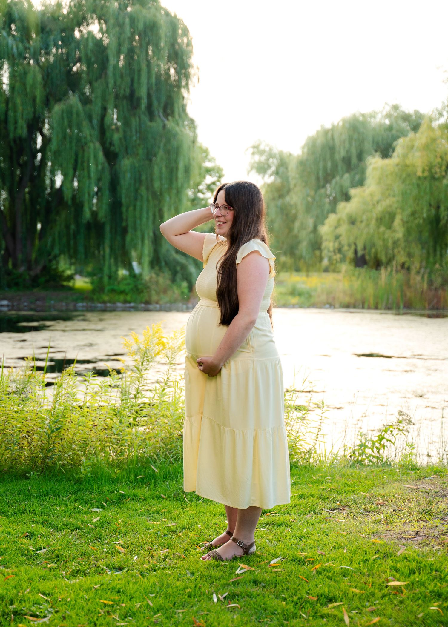 Woman in cream dress poses near pond with weeping willows in background.