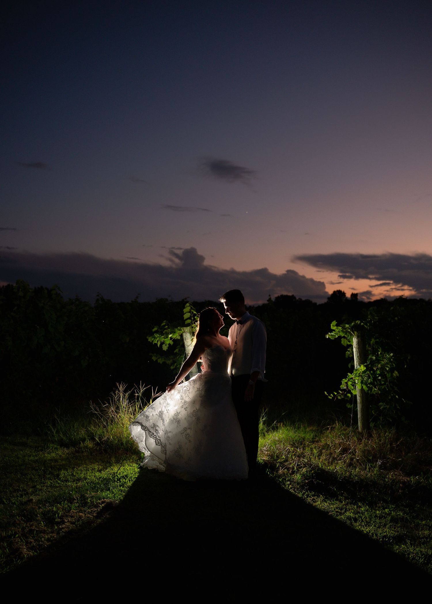 Romantic bride and groom silhouetted against a stunning sunset sky at a vineyard wedding venue.