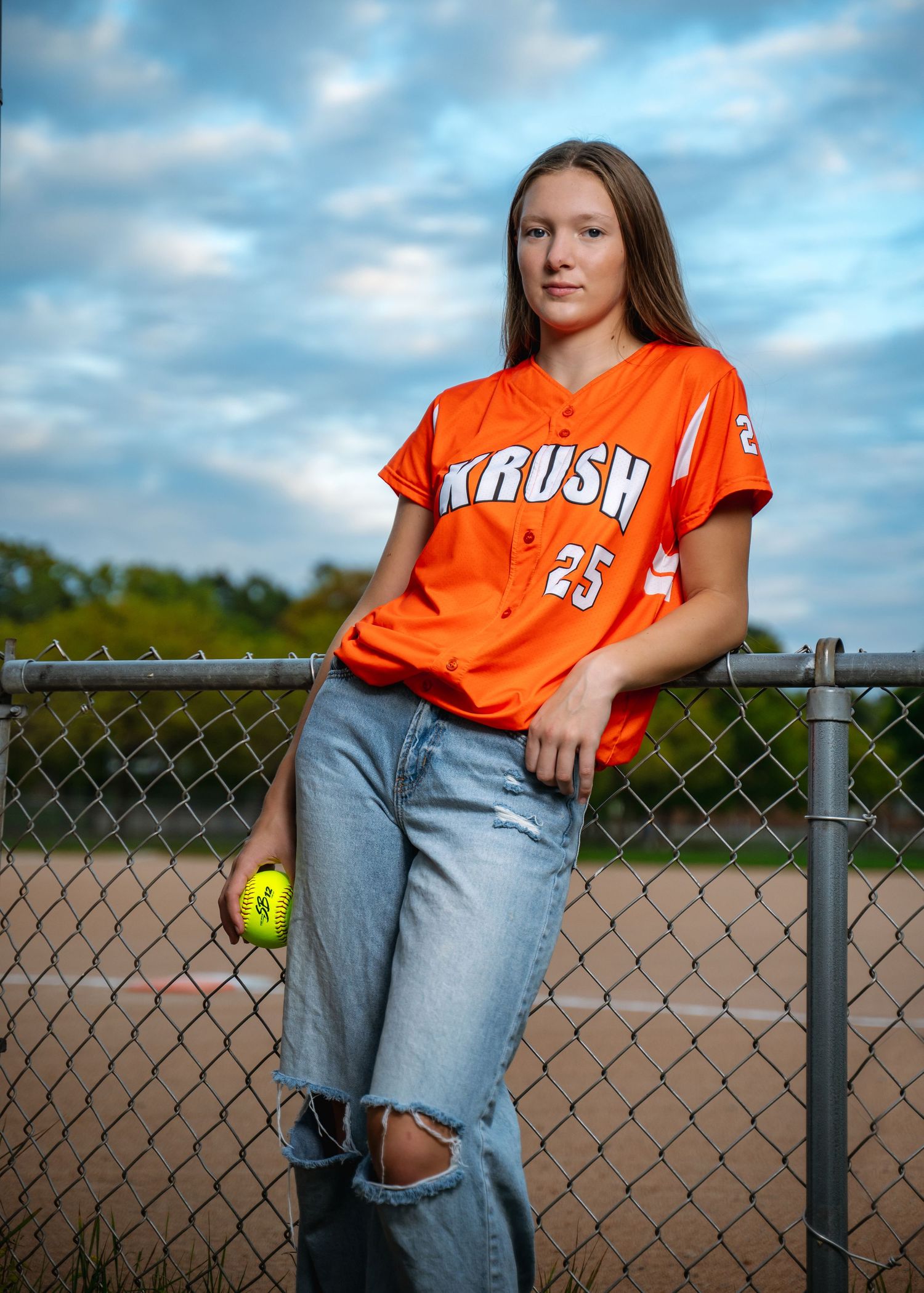 Orange softball jersey with number 25 displayed against chain link fence backdrop.