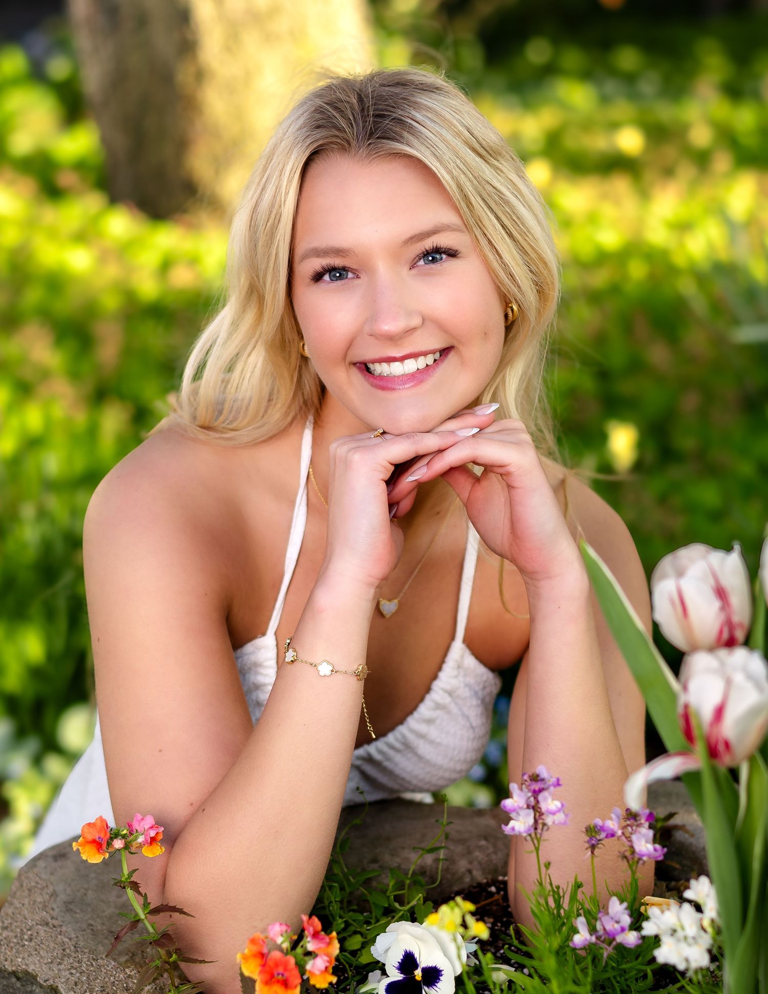 A senior portrait photoshoot in a garden with tulips and spring flowers in natural outdoor lighting.