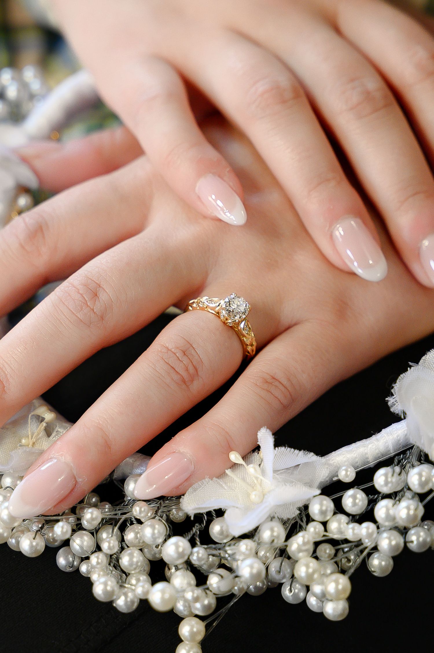A close-up of a bride's manicured hand with engagement ring resting on pearl decorations.