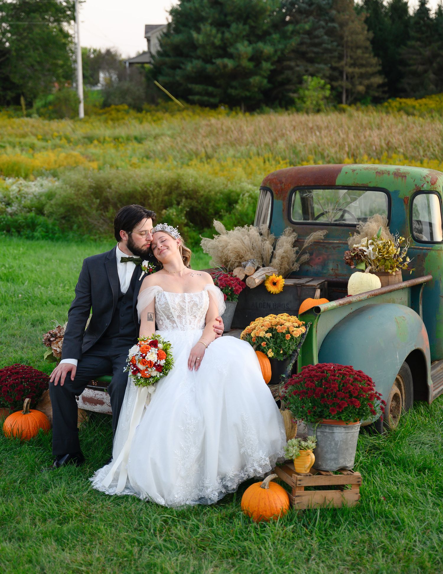 Rustic fall wedding scene with vintage truck, pumpkins, and couple in formal attire.