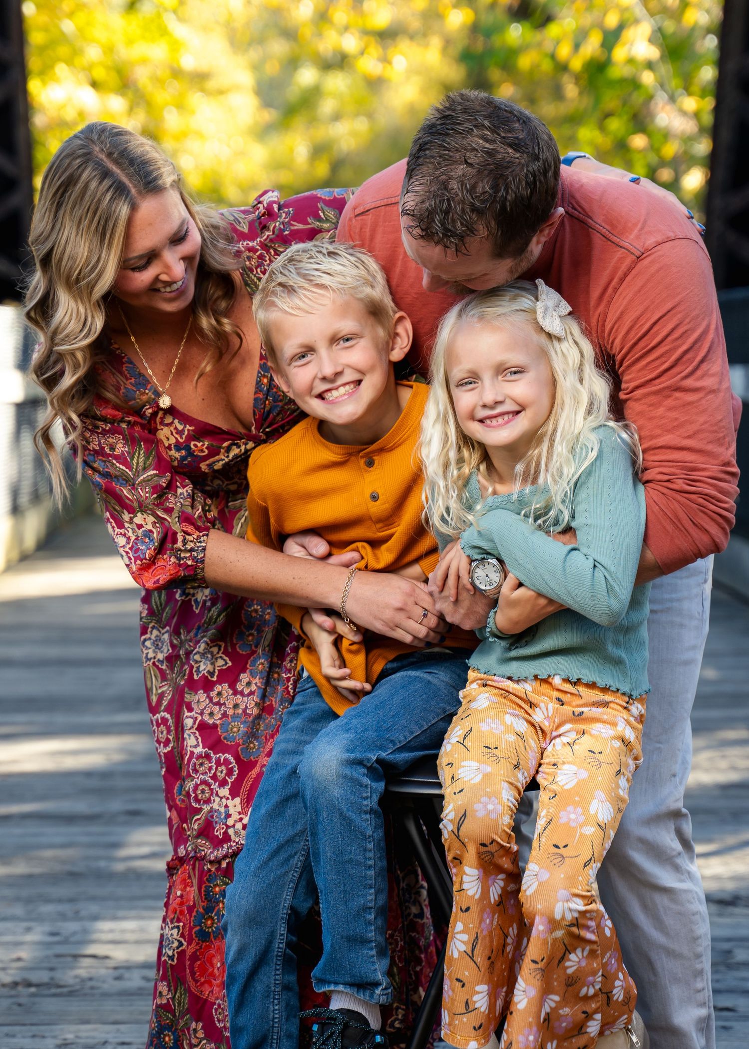 Family of four sharing joyful laughter on autumn bridge walkway.
