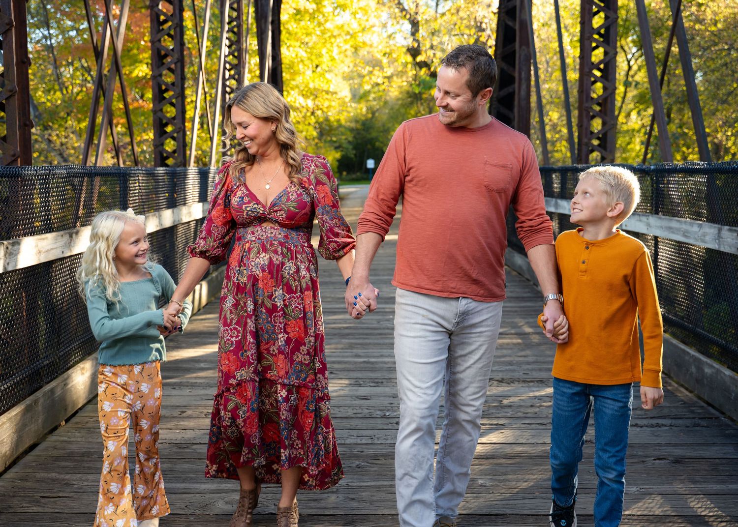 Family walking and laughing together on wooden bridge during fall season.