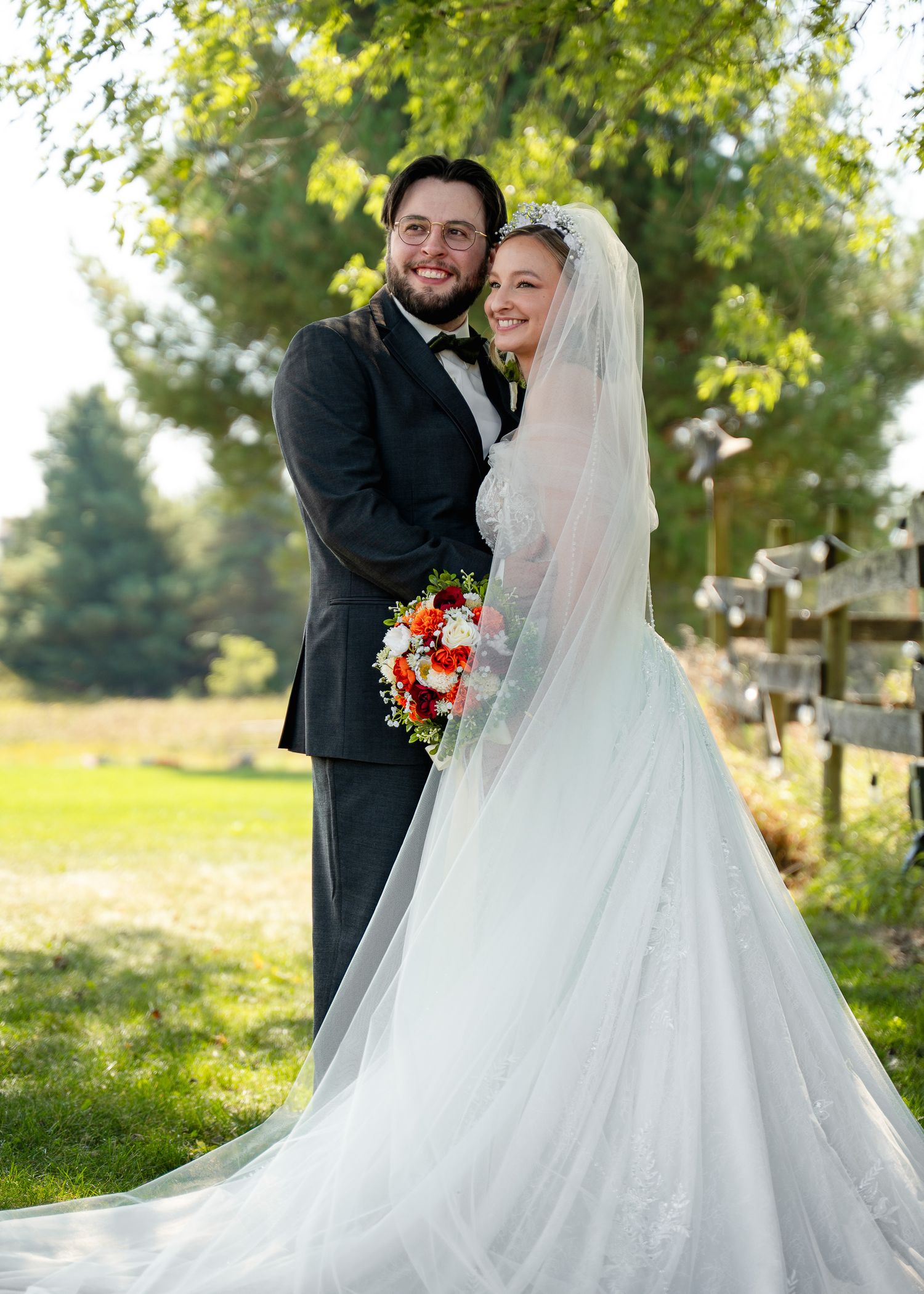 A happy couple shares a candid moment outdoors on their wedding day with lush greenery in the background.