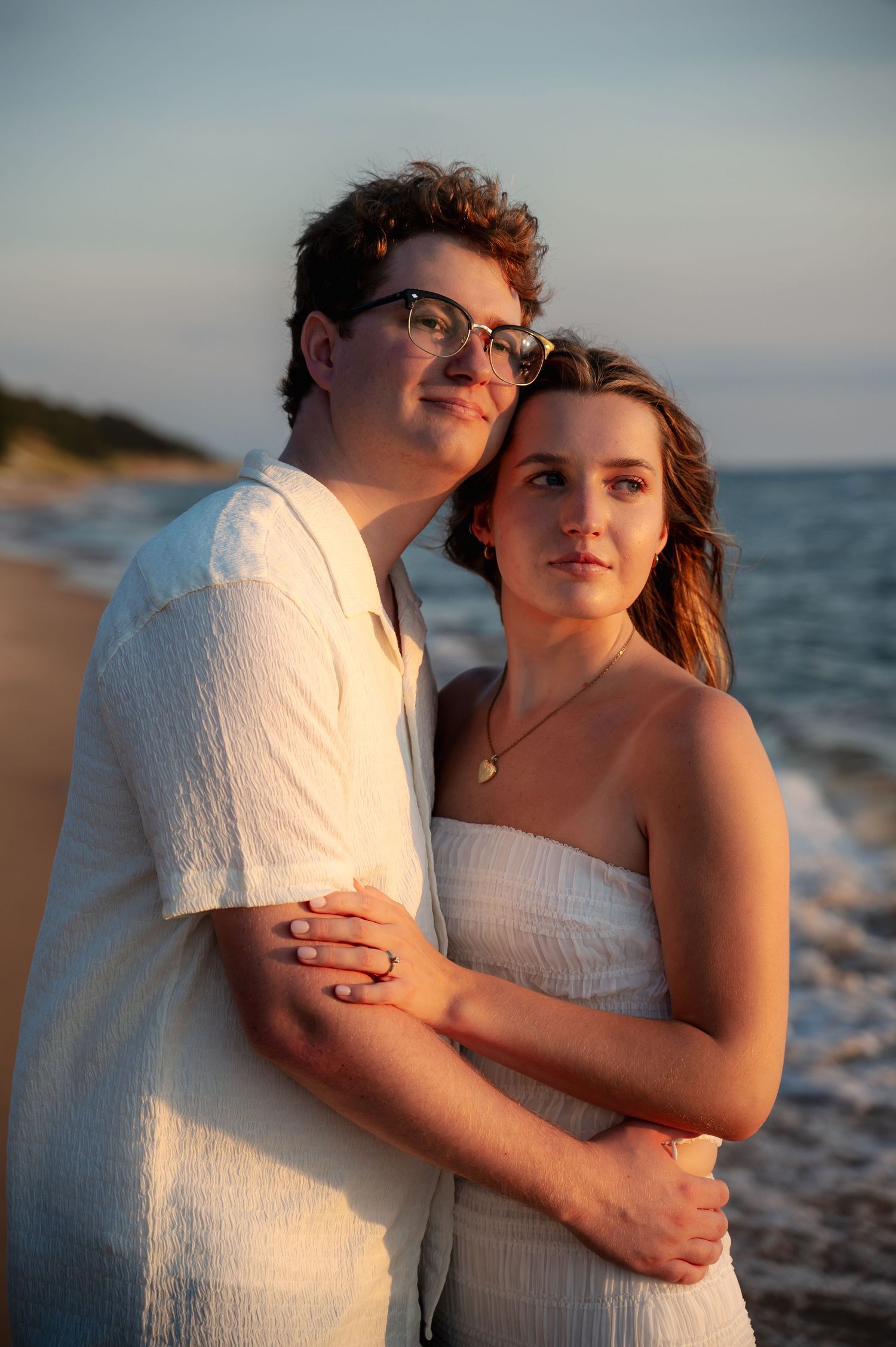 Couple in white clothing embracing on the beach during golden hour with ocean in background.