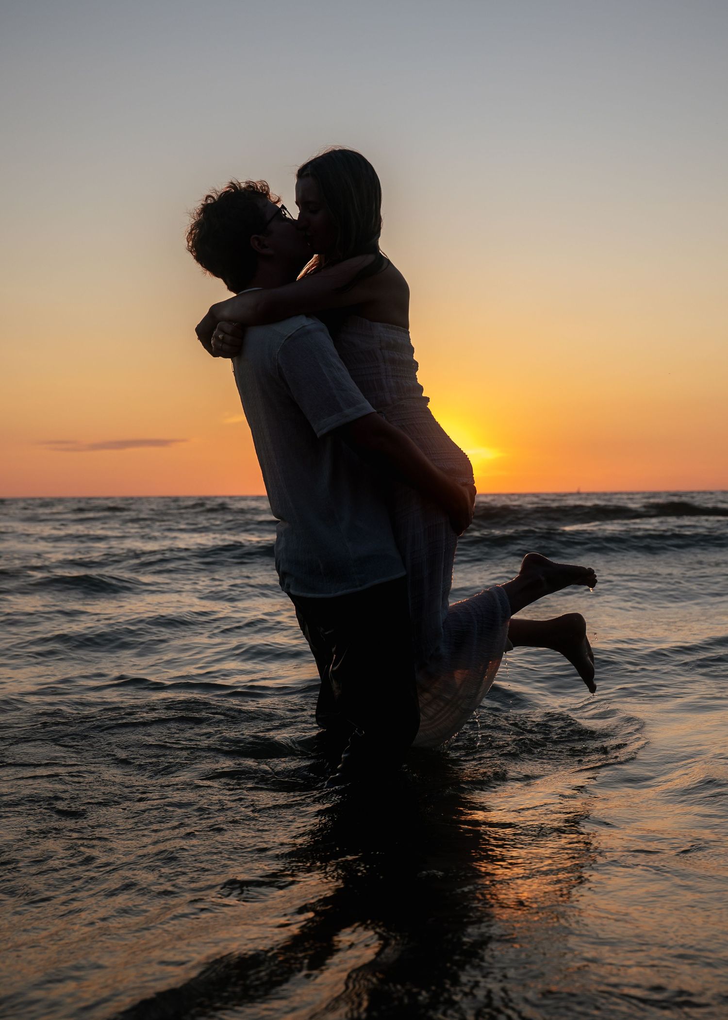 Silhouettes of a couple playing in the ocean waves at sunset.