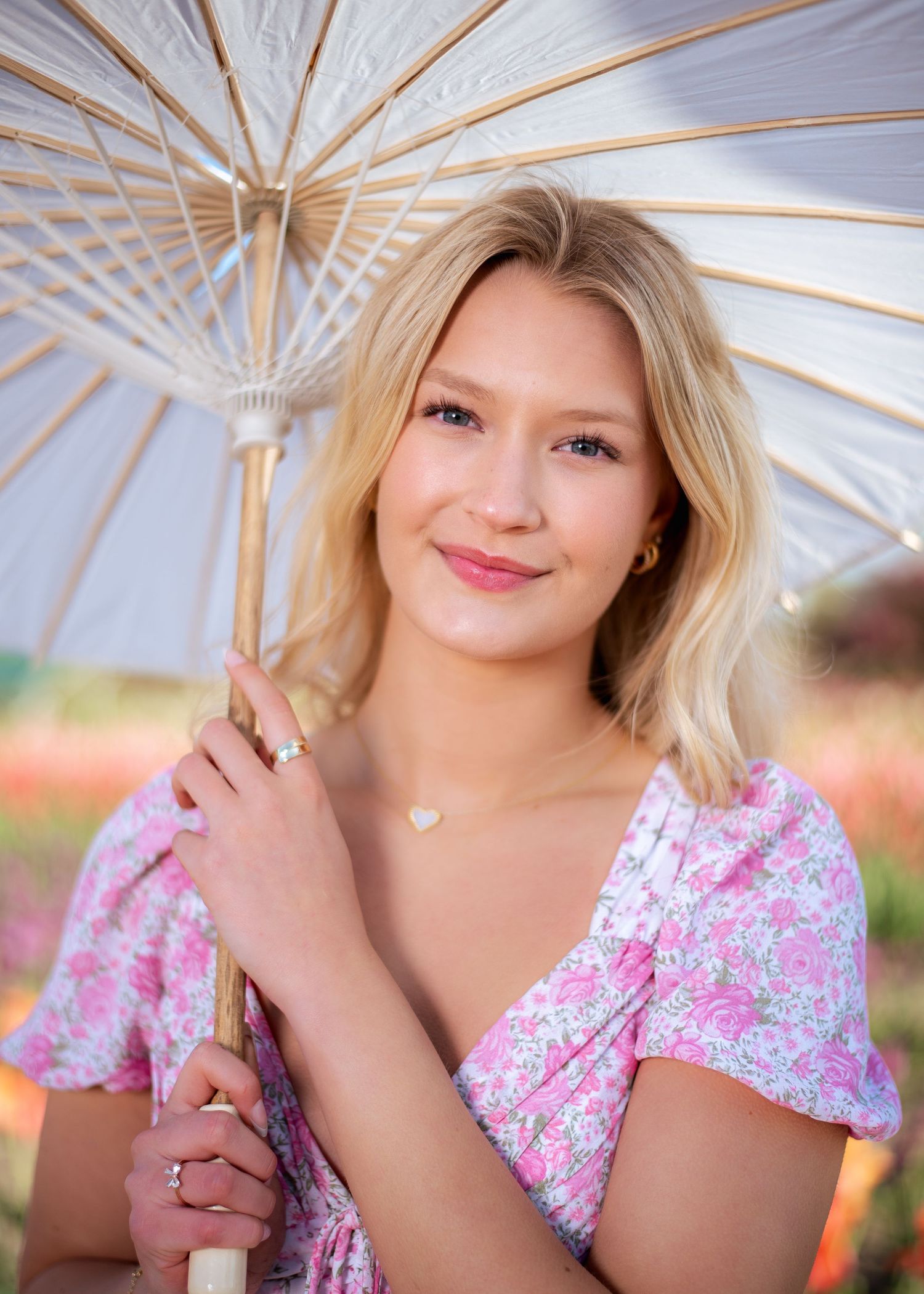 Elegant portrait under white parasol with pink floral dress in garden setting.