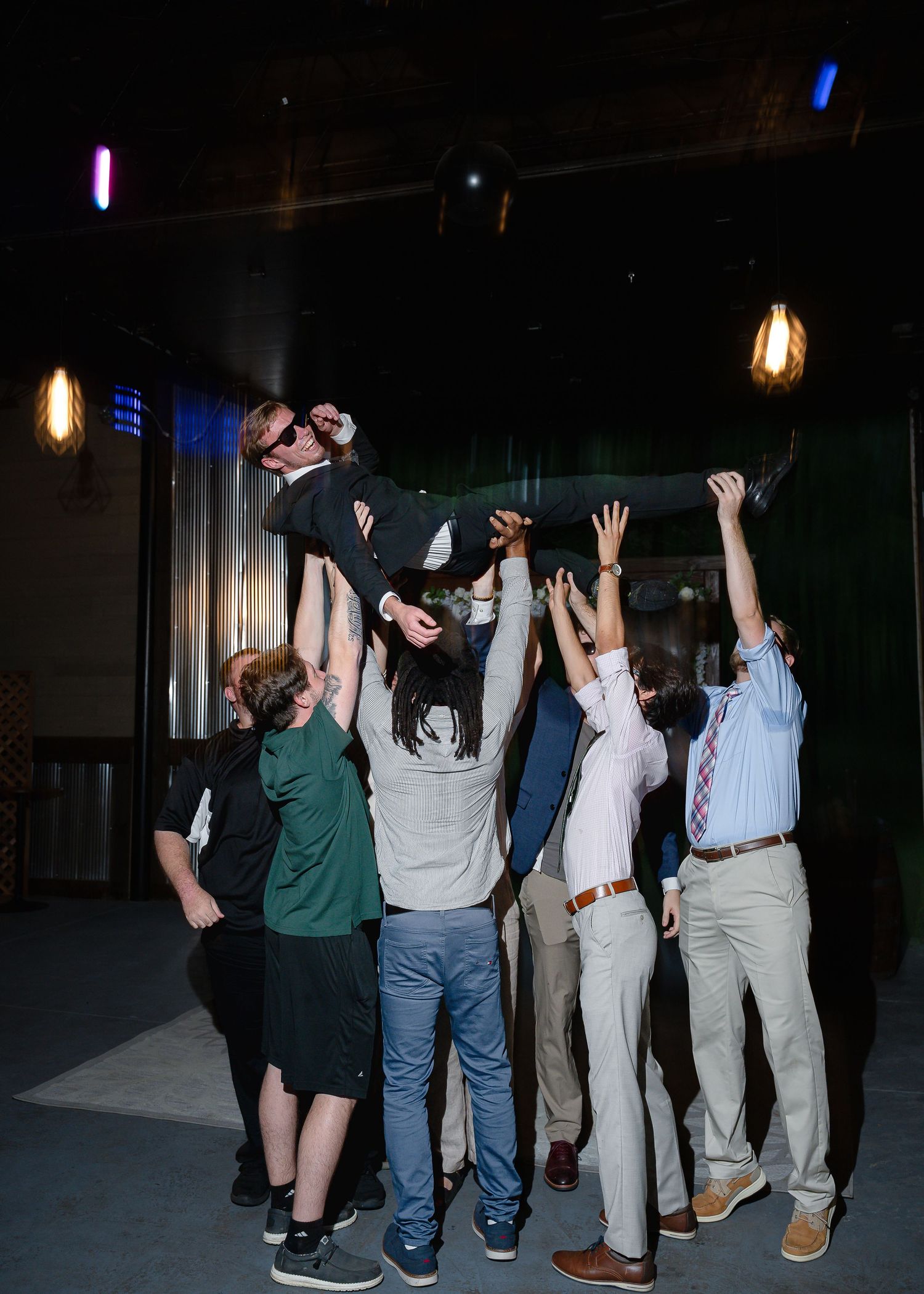 Group of people lifting a person overhead at an indoor celebration event with warm ambient lighting.