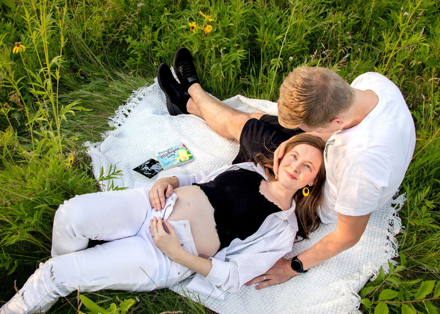 Couple sharing tender moment during outdoor maternity photoshoot in flowery meadow.