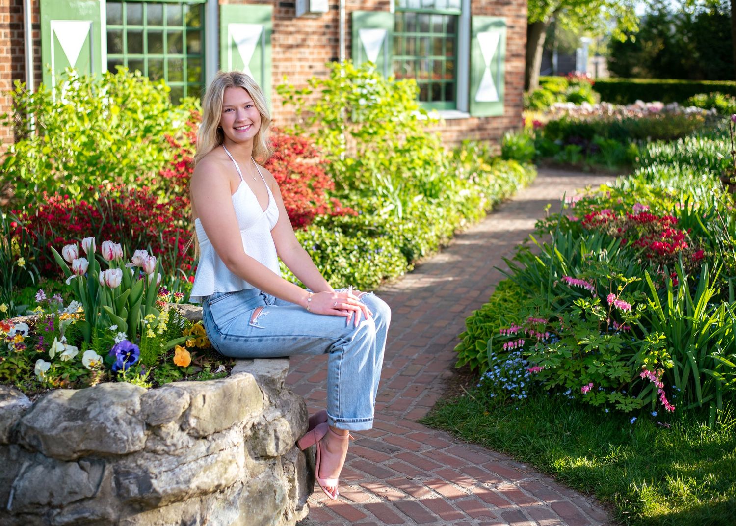 Garden path with brick walkway and blooming flowers beside stone wall.