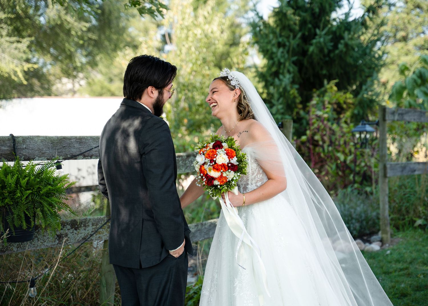 Newlyweds share a moment in a garden setting with white fence and greenery in background.
