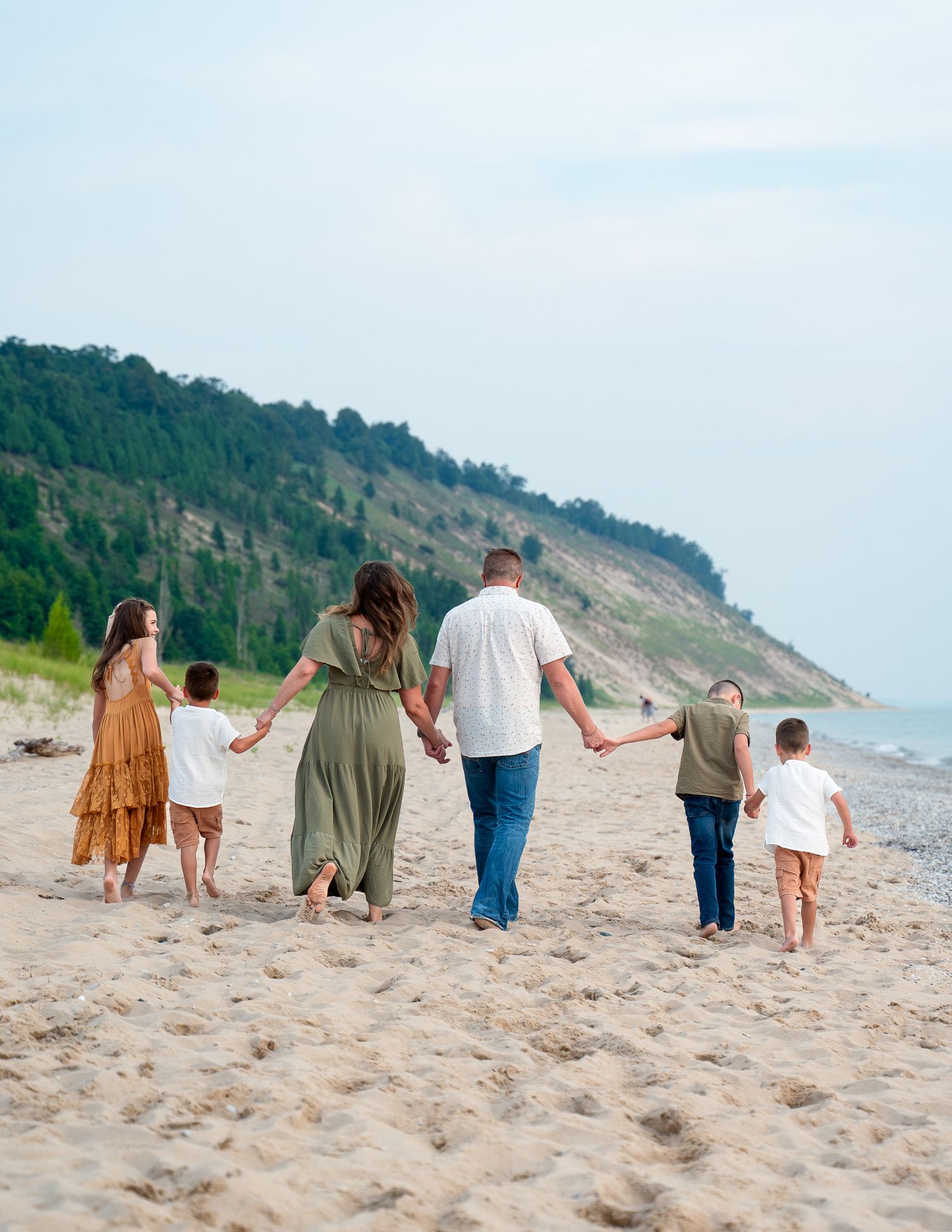 Family walking together holding hands on a sandy beach with cliffs in the background.