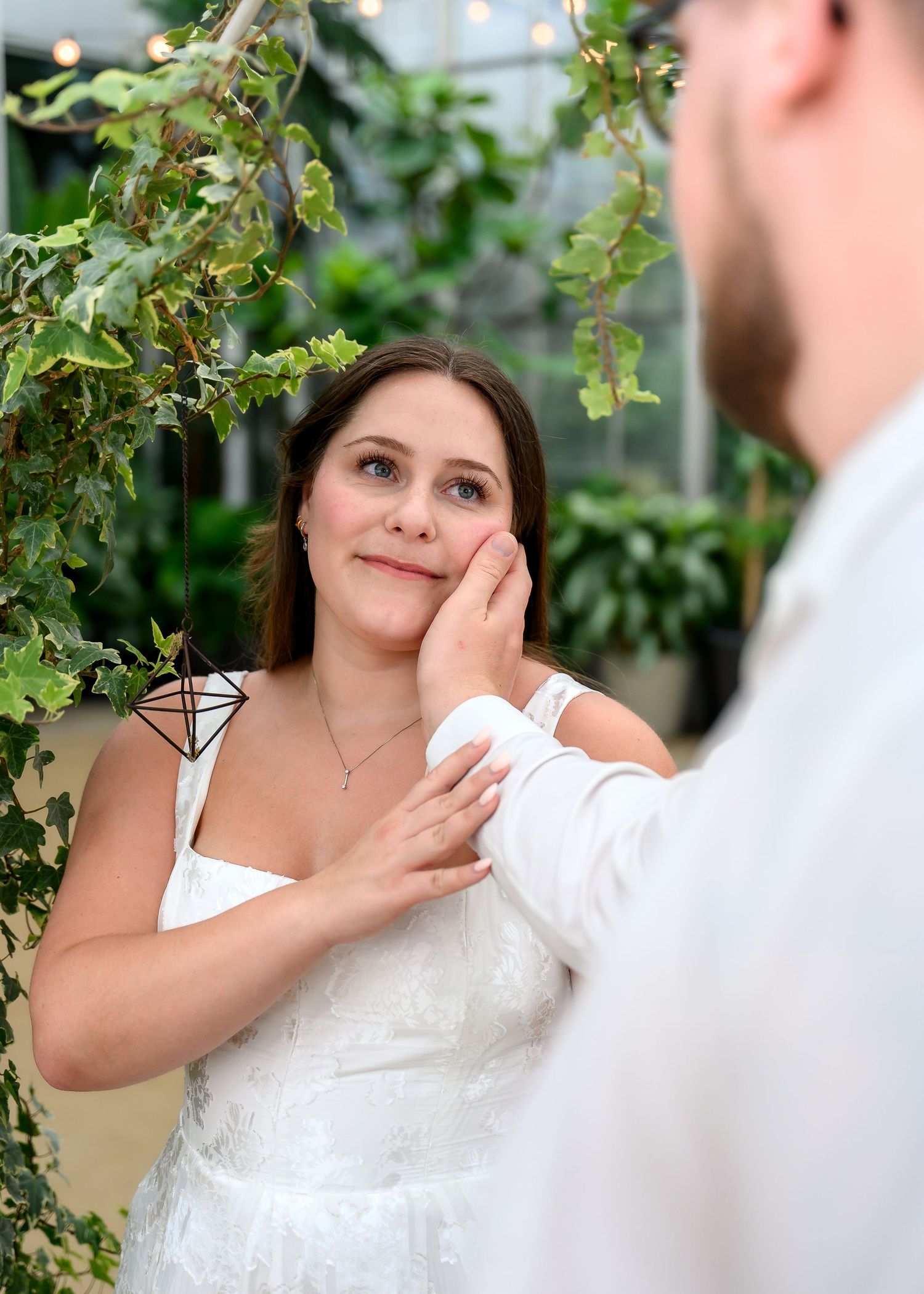 A tender moment between a bride in white dress and groom as he gently touches her face in a garden setting.