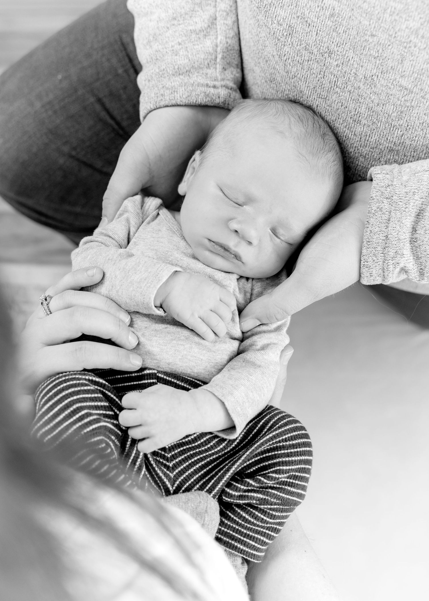 A sleeping baby in striped pants is photographed in black and white on a soft surface.