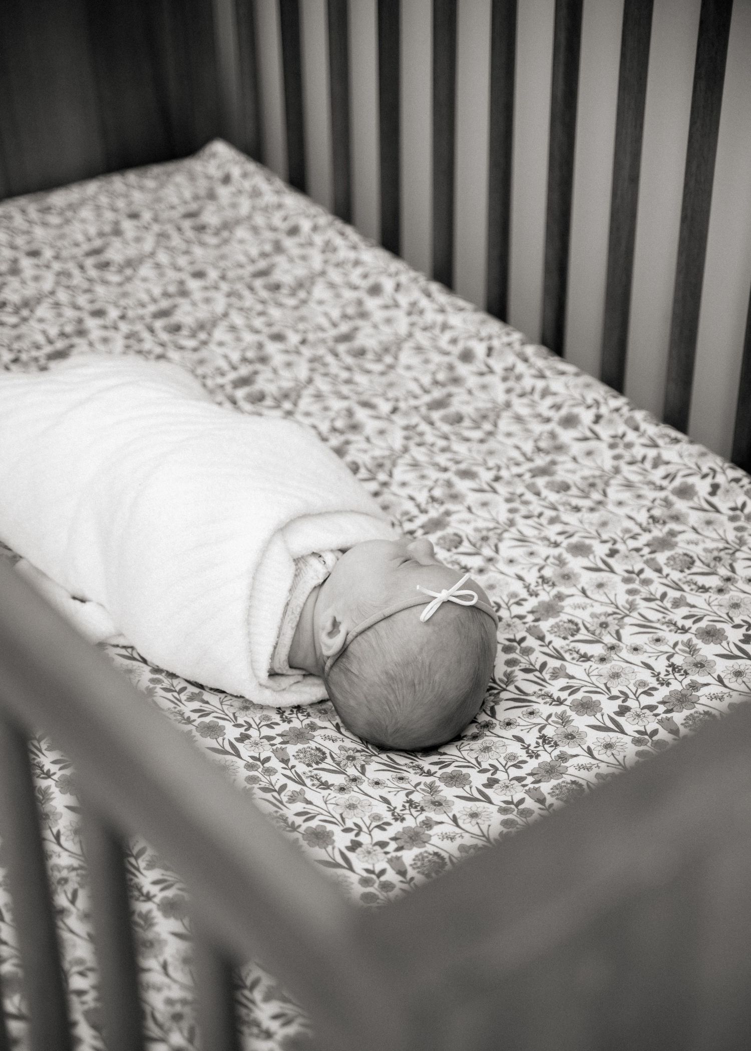 A sleeping newborn baby rests on a patterned crib sheet in black and white.