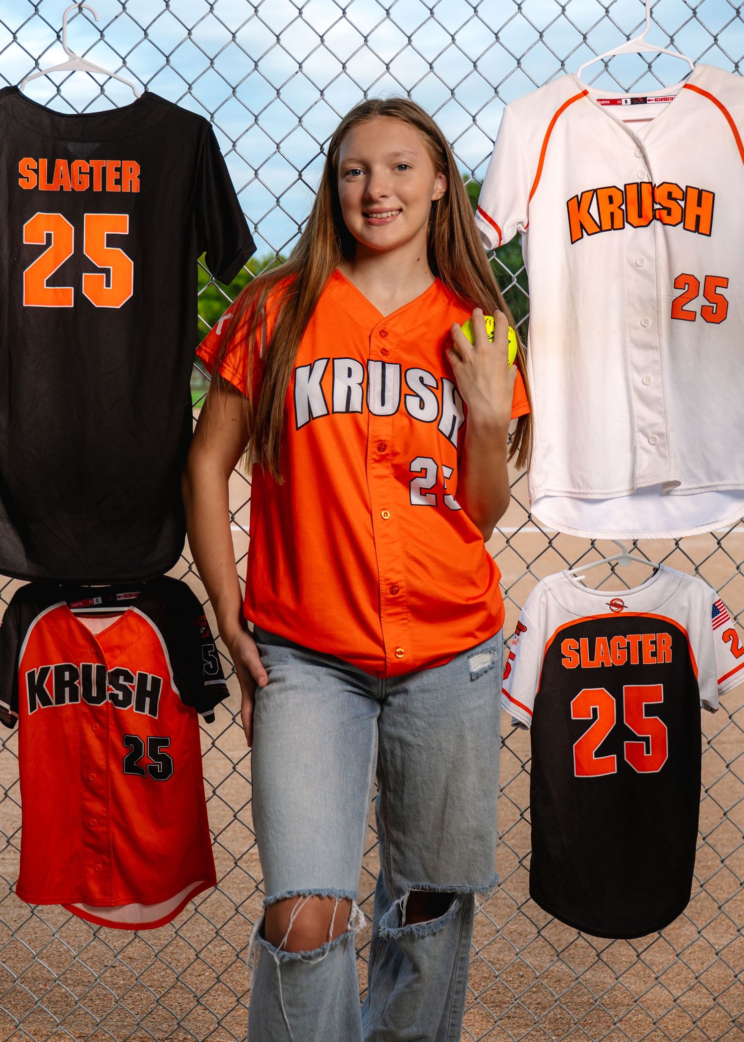 Collection of orange and black softball jerseys with number 25 hanging on fence.