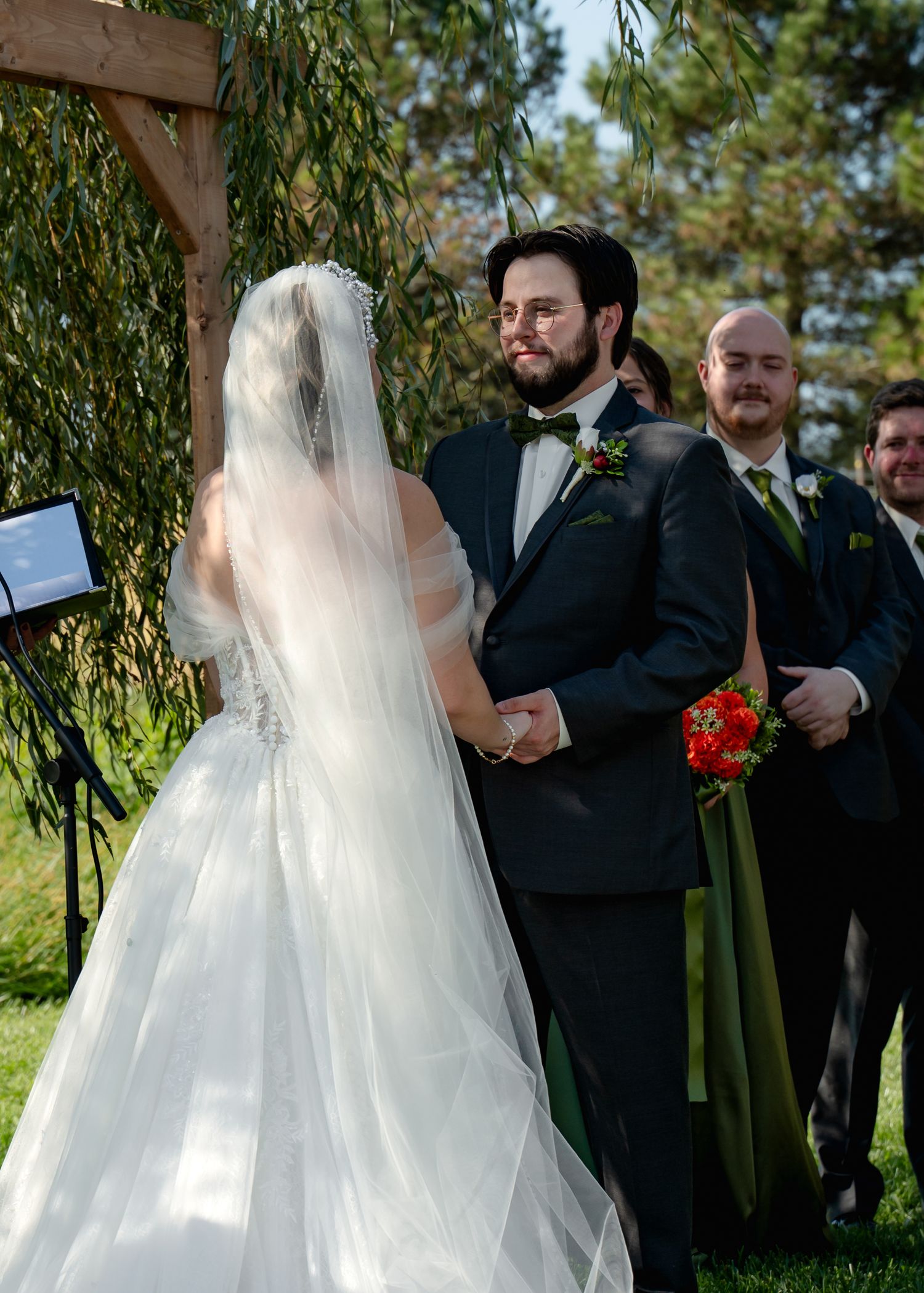 Intimate wedding ceremony moment under a willow tree with floral arch decorations.