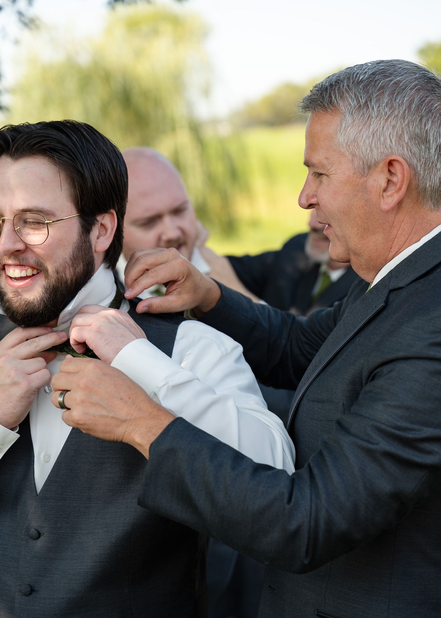 Groomsmen in dark suits playfully pose together outdoors.