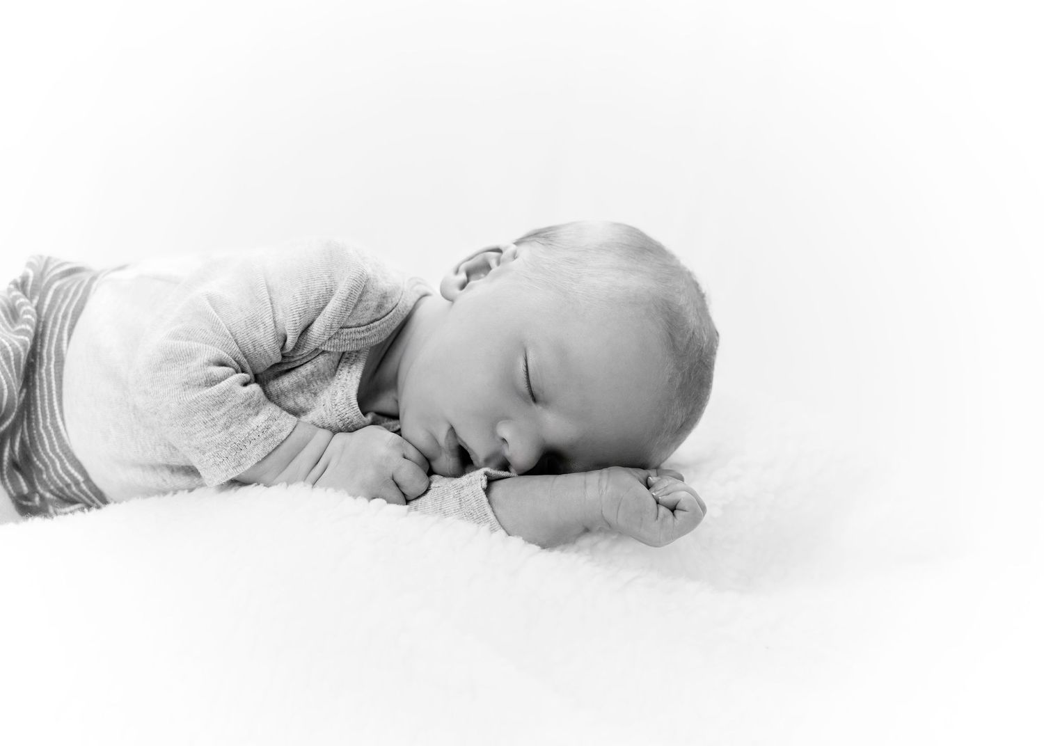 Black and white artistic photos of a sleeping newborn baby in soft lighting.