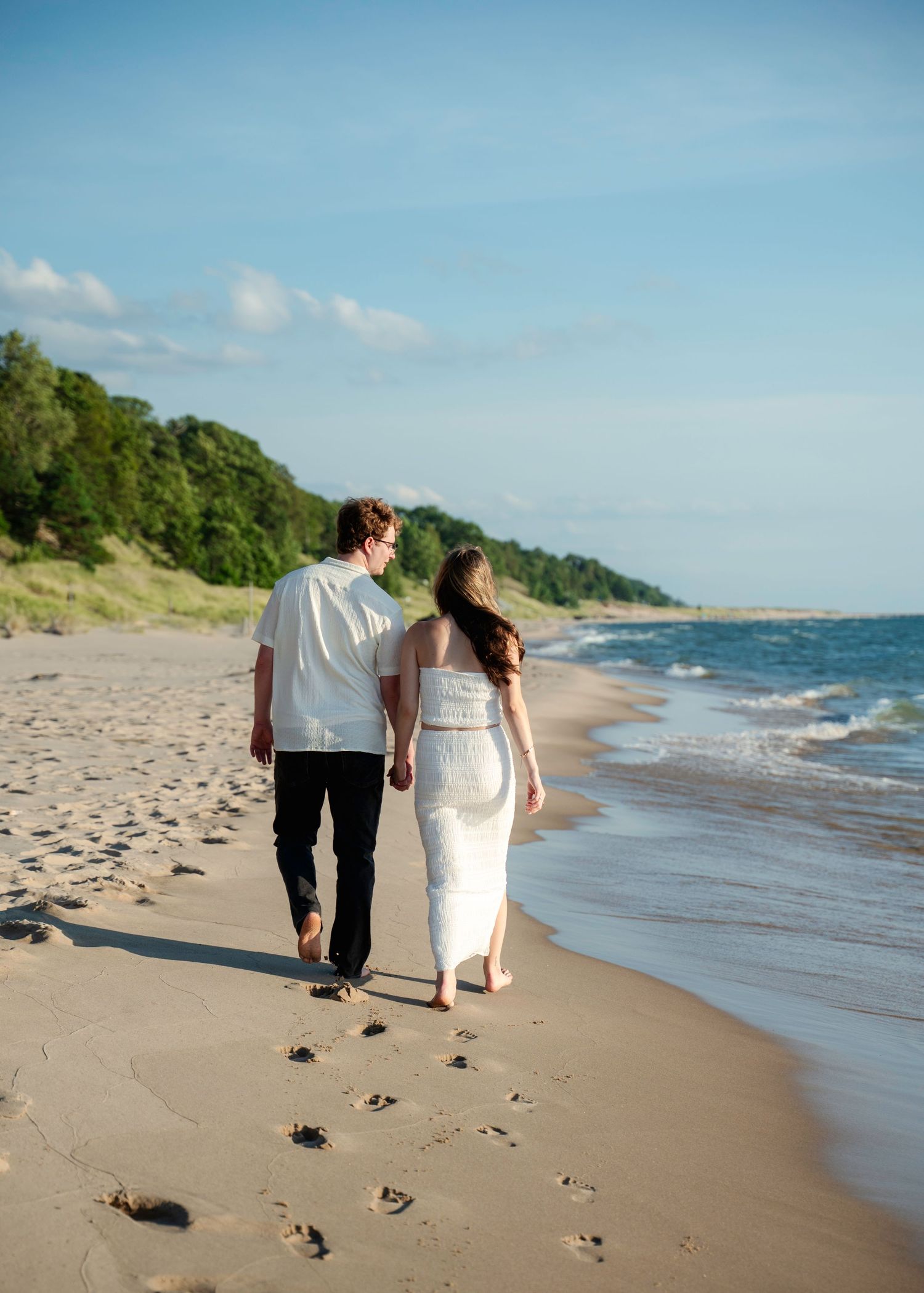 Couple walking hand in hand along a scenic beach shoreline on their wedding day.