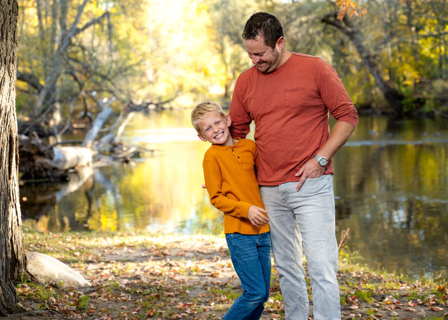 Candid laughter between parent and child during autumn photoshoot by water.