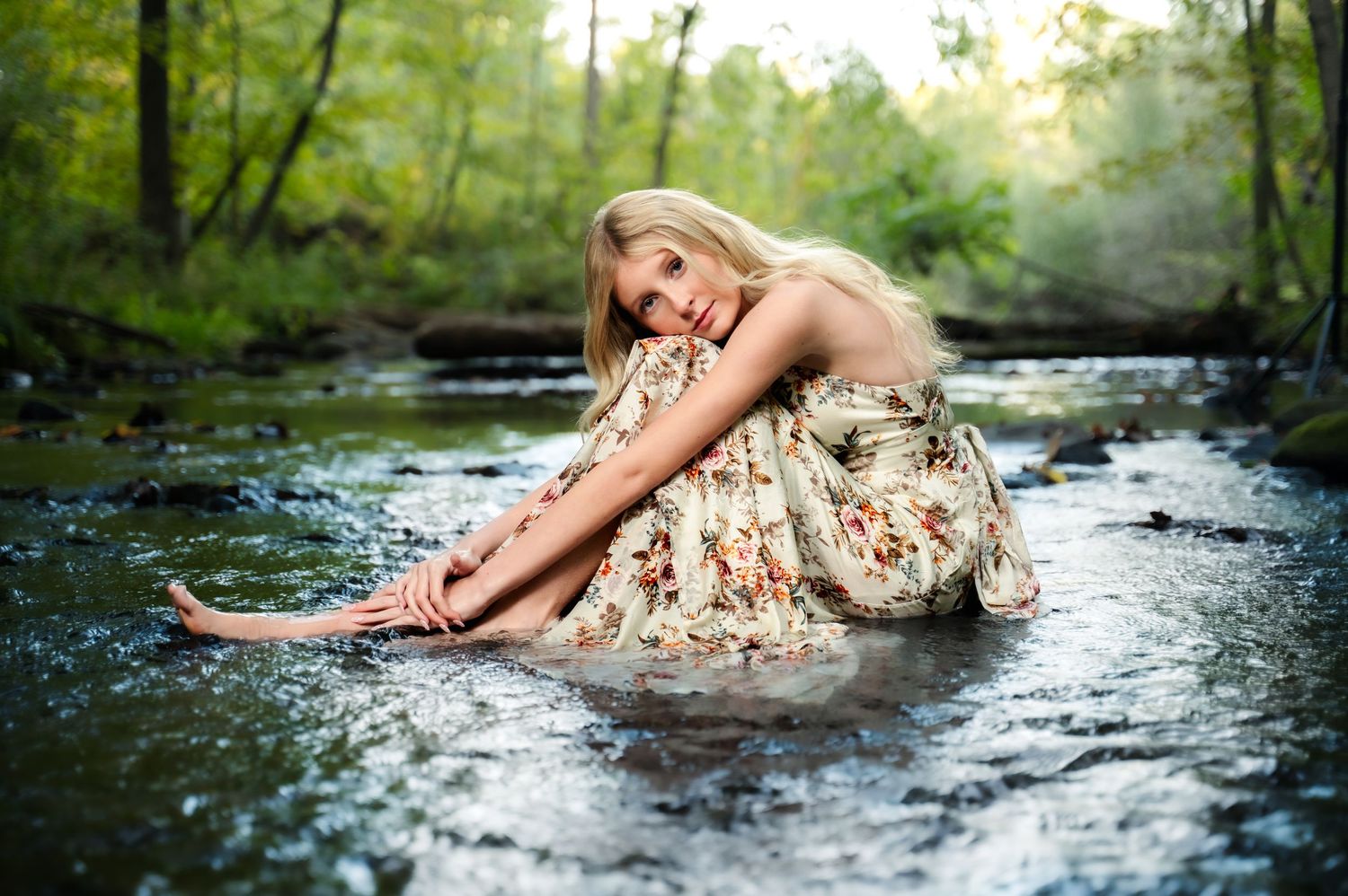 Person in floral dress lying in shallow stream water during outdoor photo session.