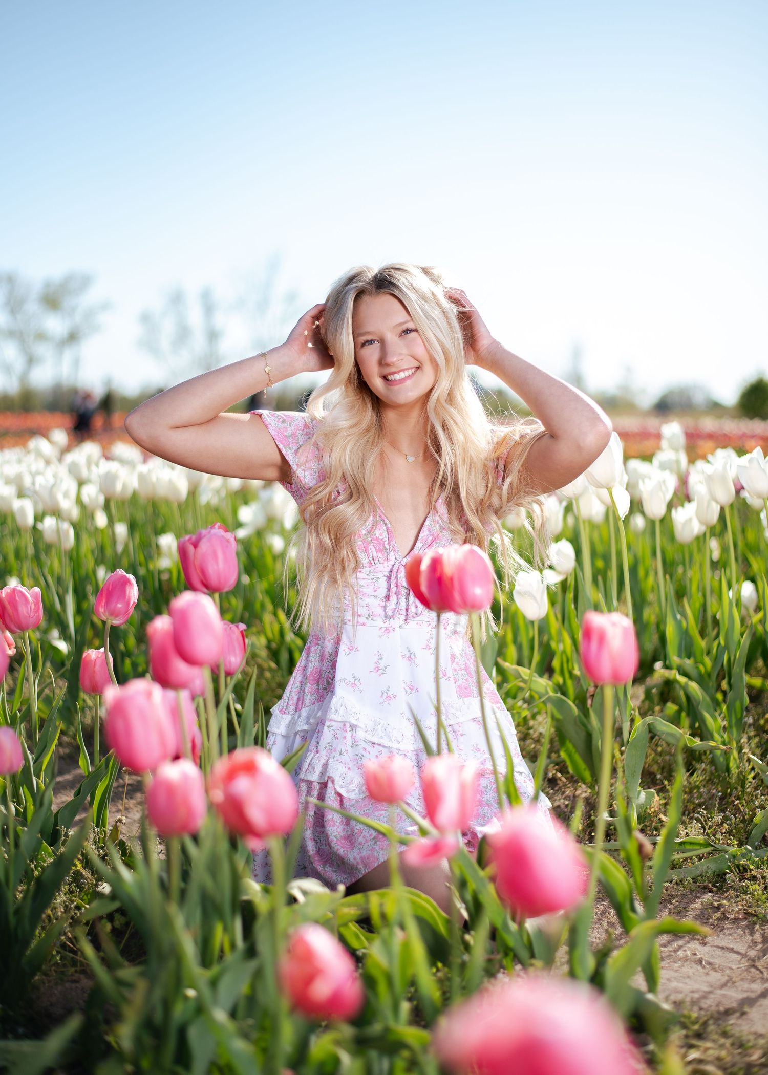 Woman in white dress poses joyfully among vibrant pink tulips in a spring garden field.