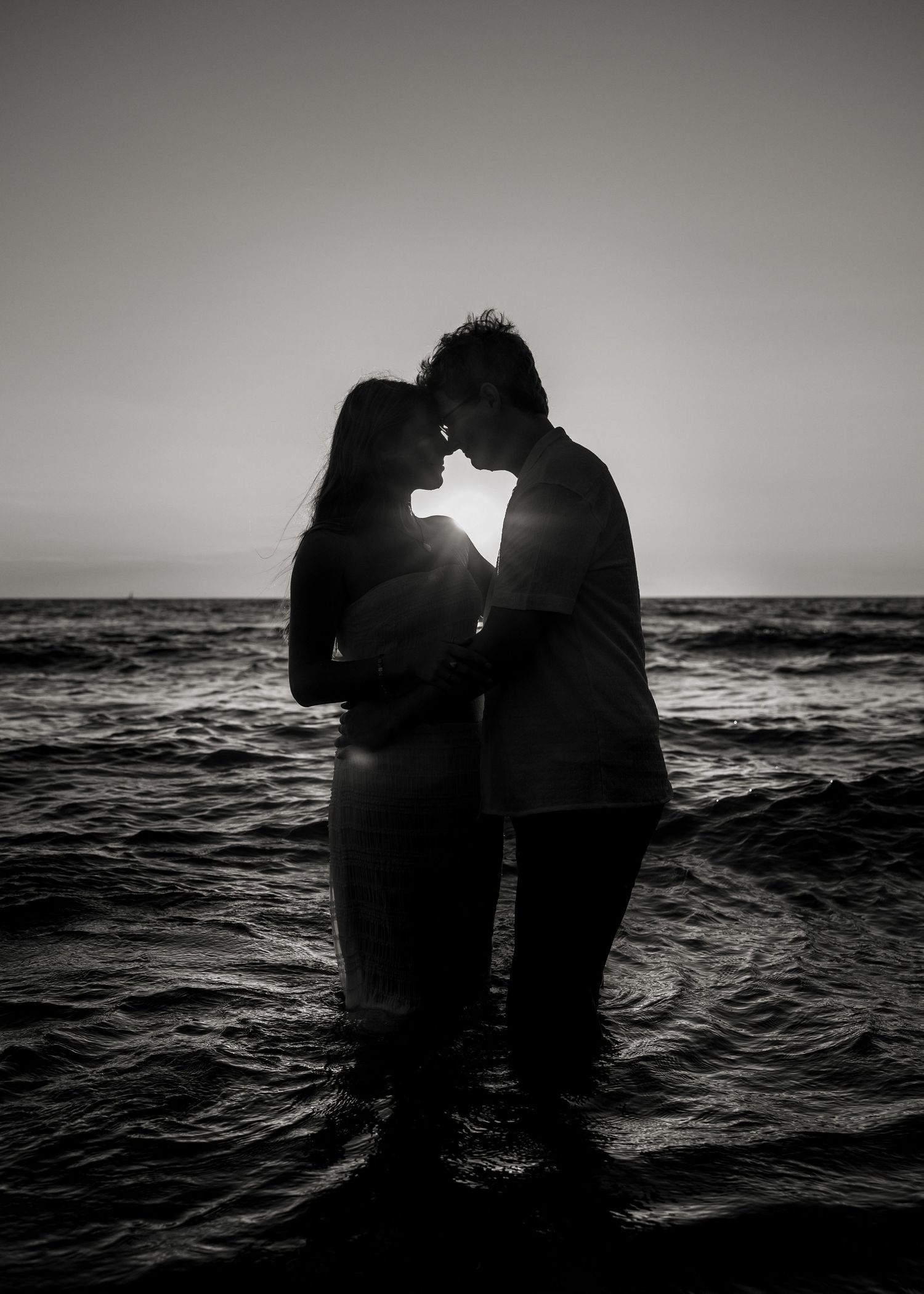 Romantic silhouettes of a couple embracing against a dramatic ocean sunset backdrop.