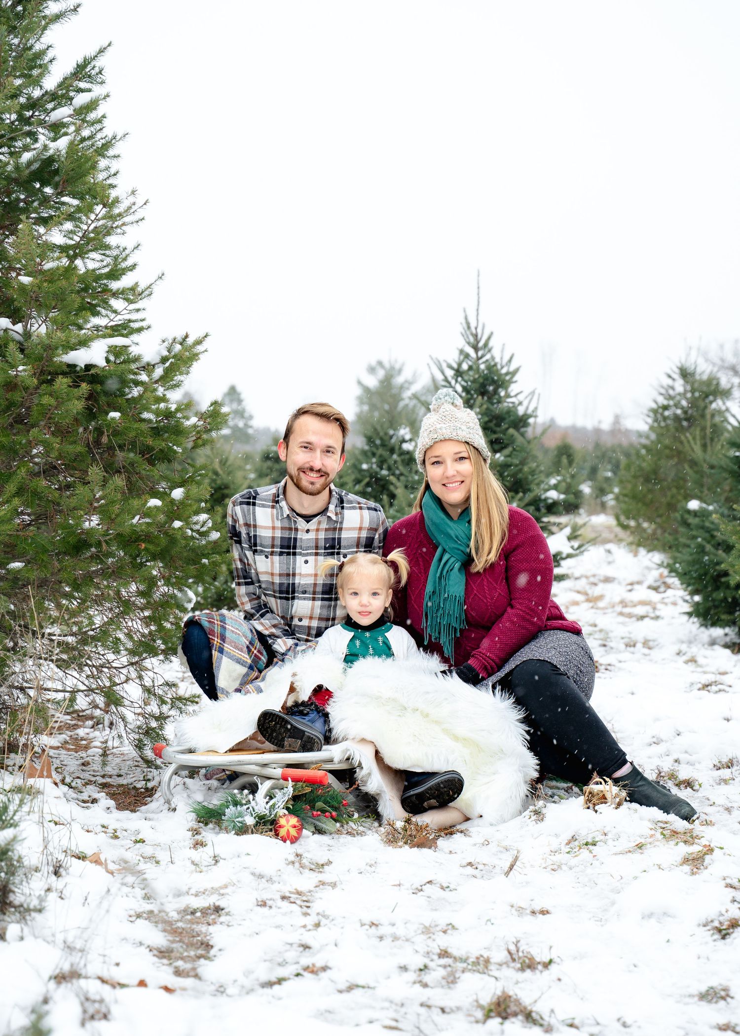 Winter family scene on a sled with snow-covered pine trees.