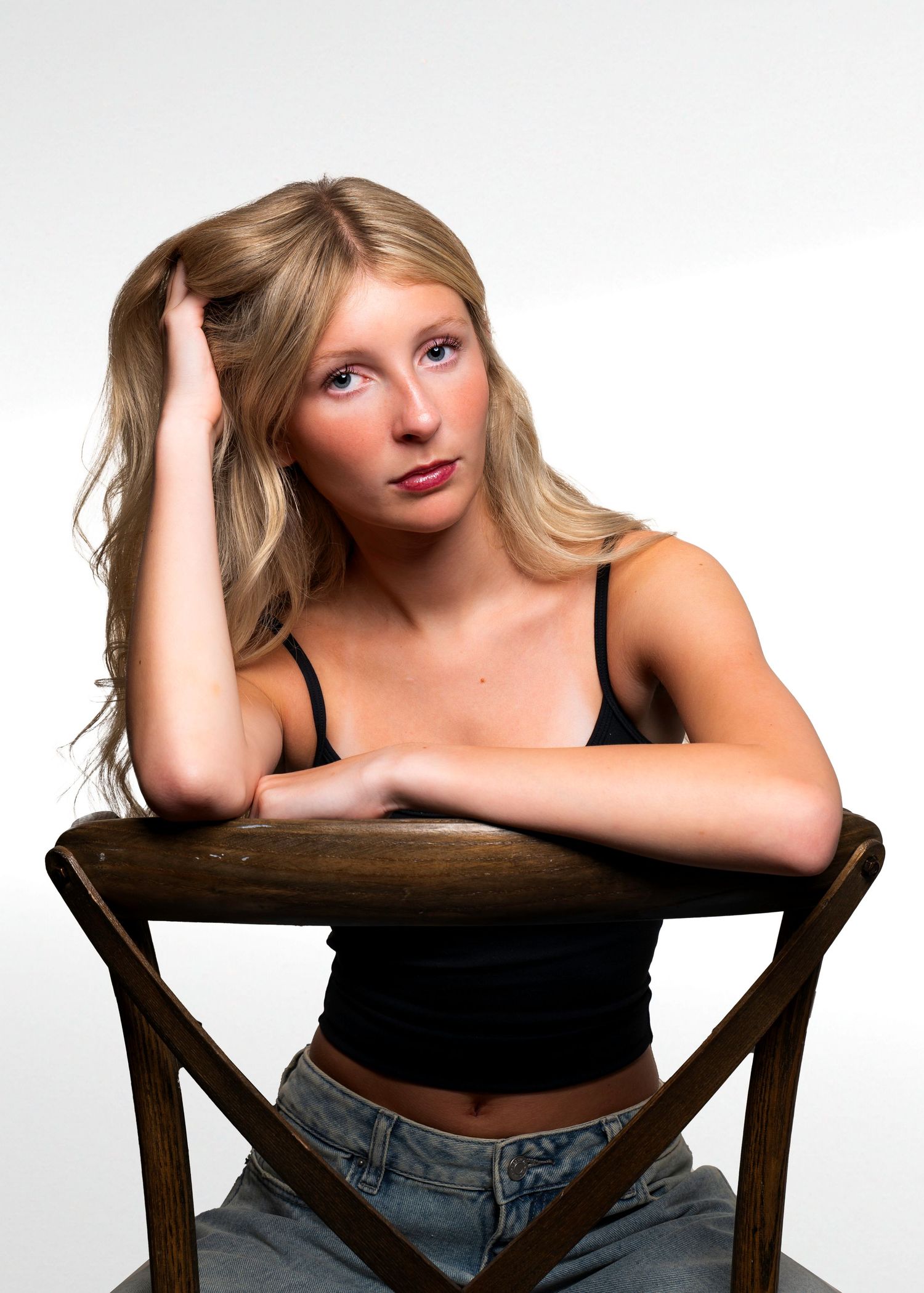 Multiple poses on a wooden chair wearing black top and jeans in studio setting.