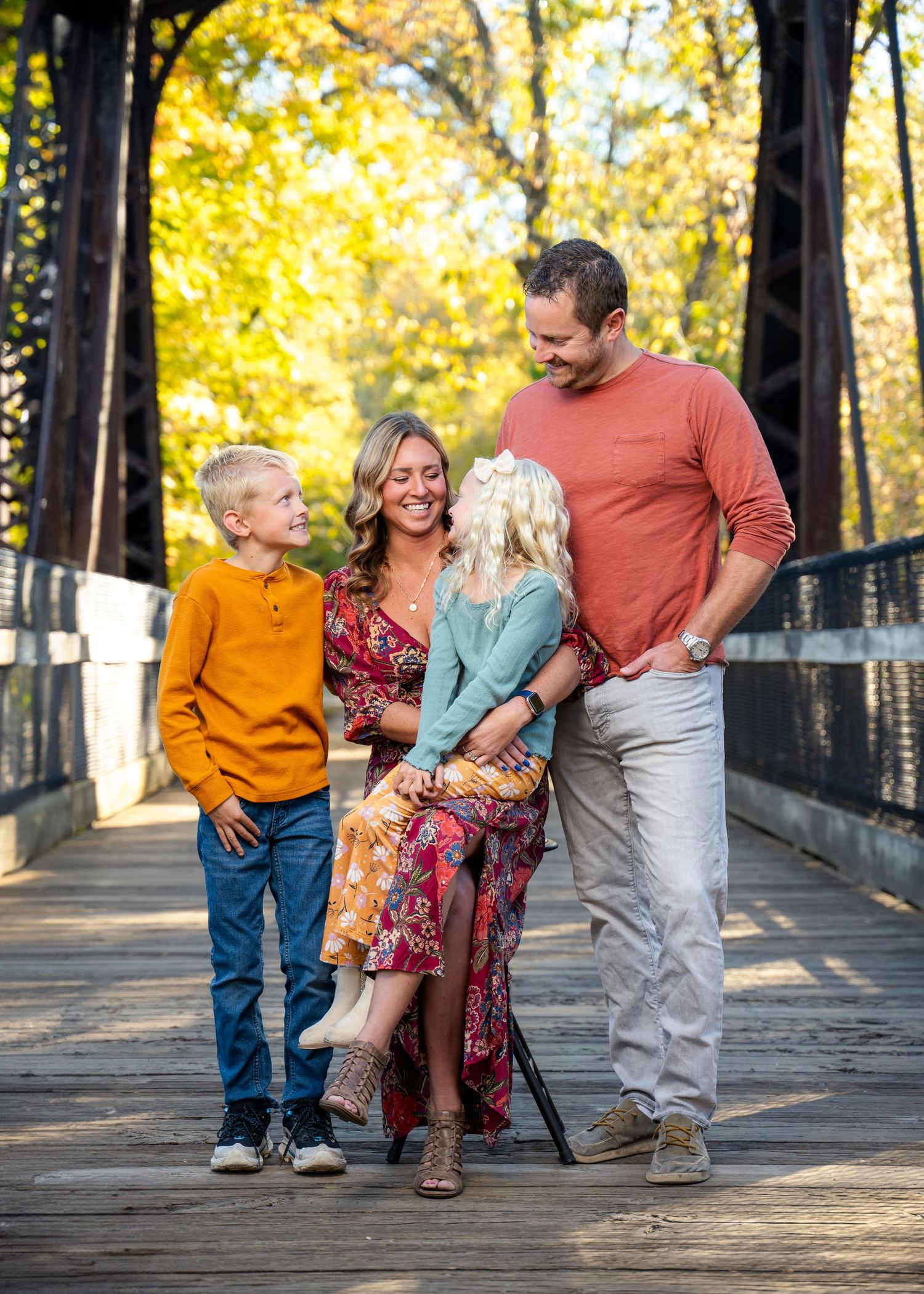 Family walking and laughing together on a wooden bridge surrounded by autumn trees.