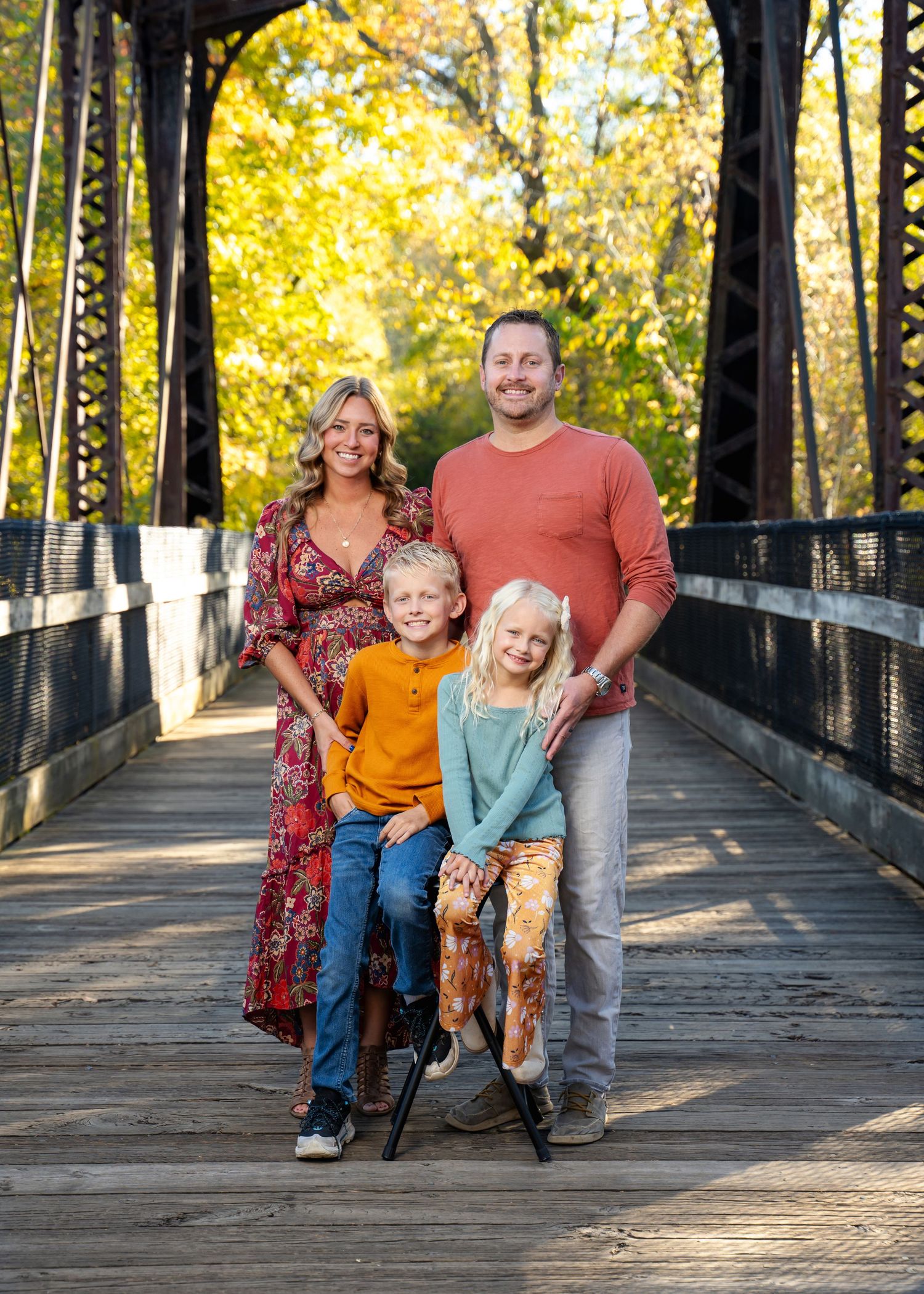 Family portrait on a wooden bridge with golden autumn trees in the background.