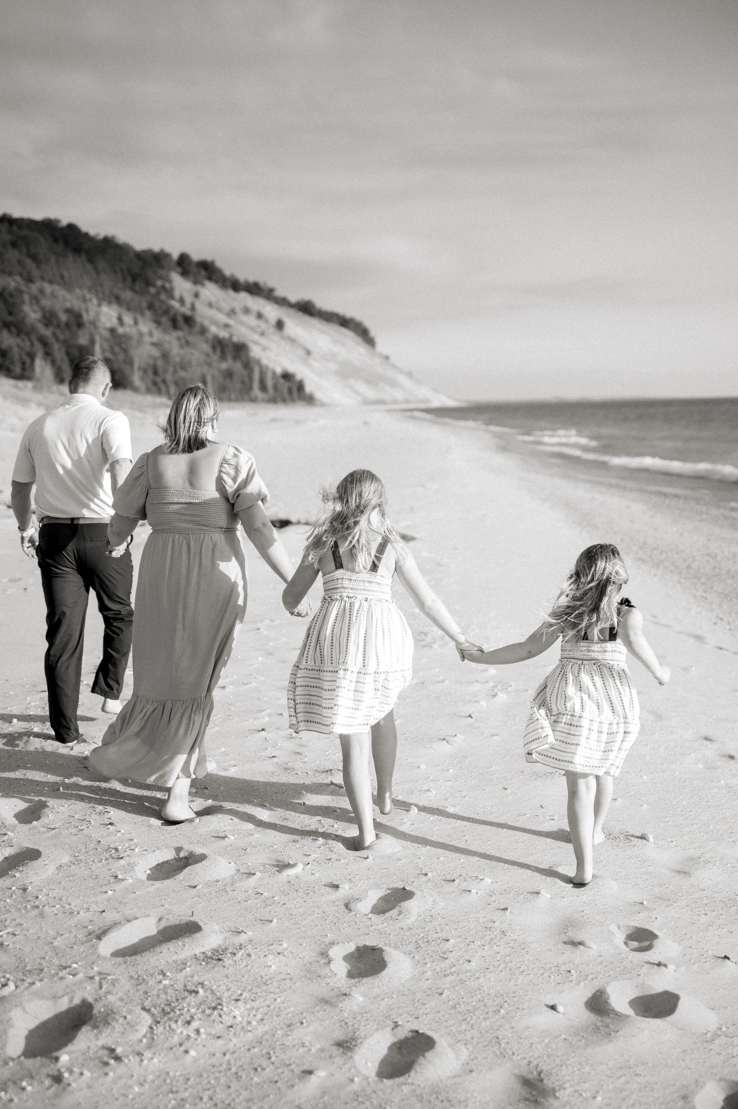 Family holding hands while walking along a scenic beach in black and white.