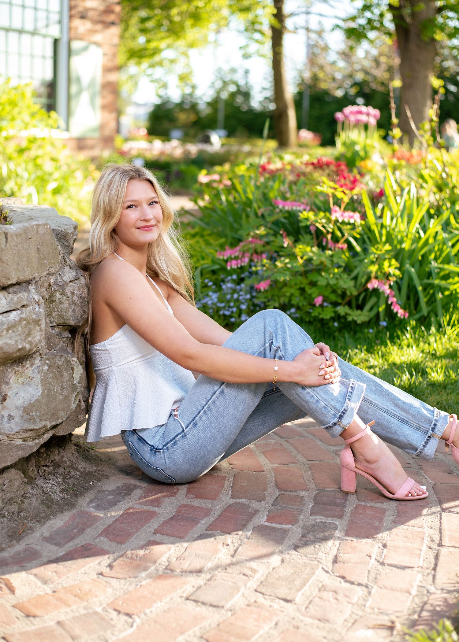 Woman in casual attire relaxes on brick pathway near garden wall.