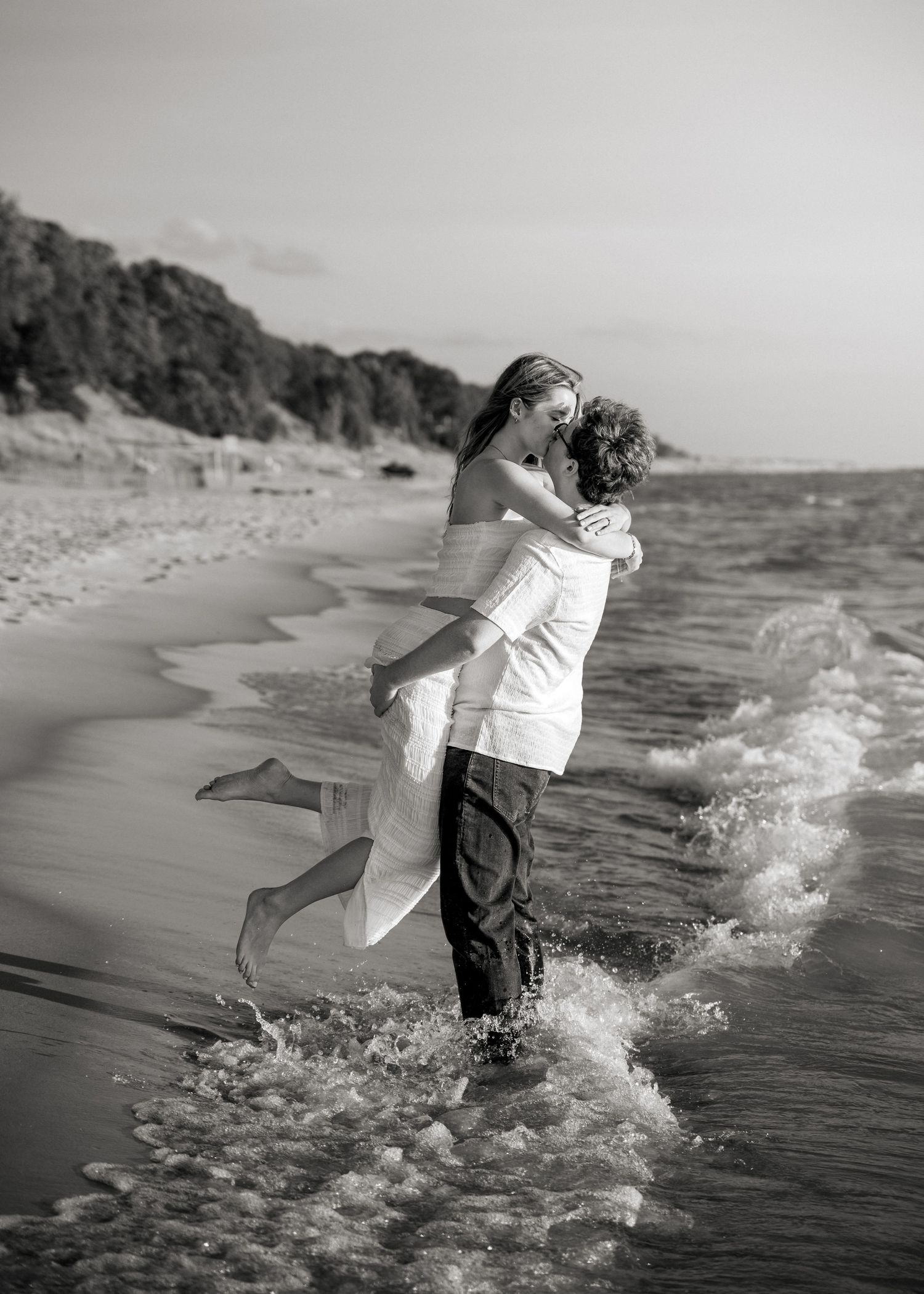 Black and white photo of a playful couple splashing in ocean waves.